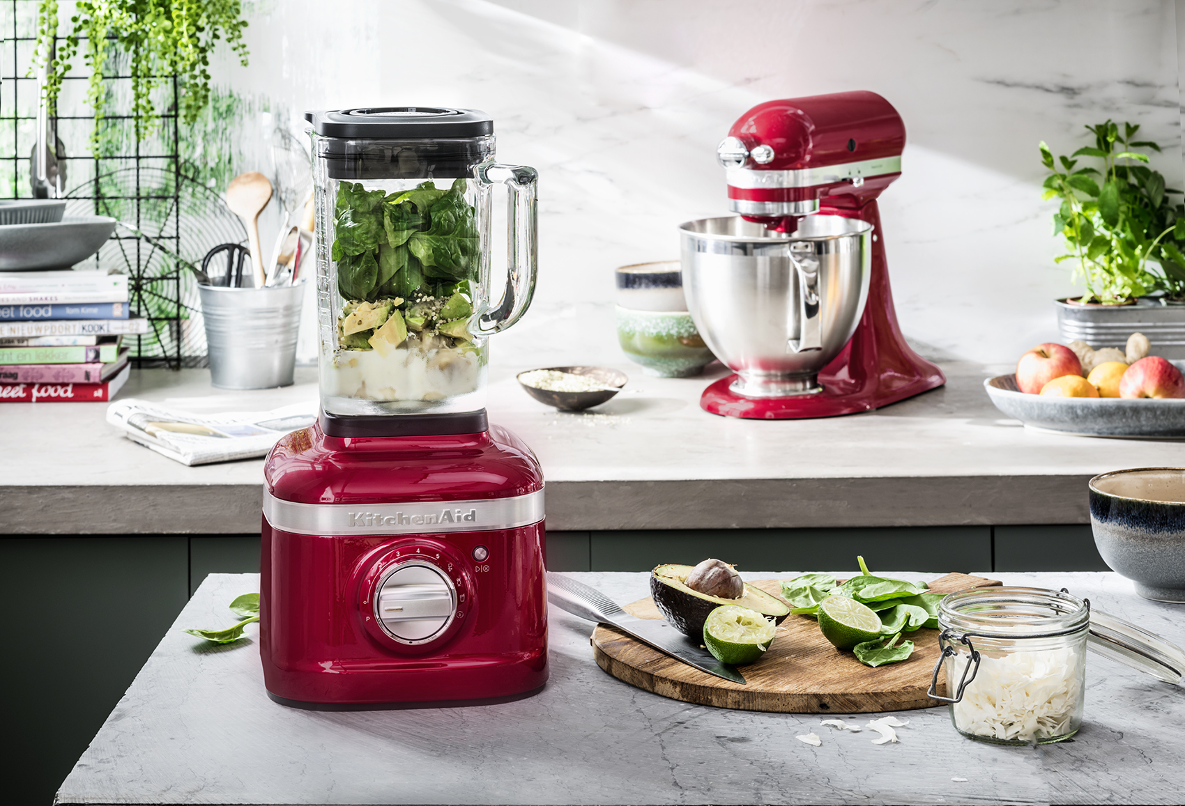 Una licuadora roja KitchenAid con ingredientes y otros elementos de cocina.