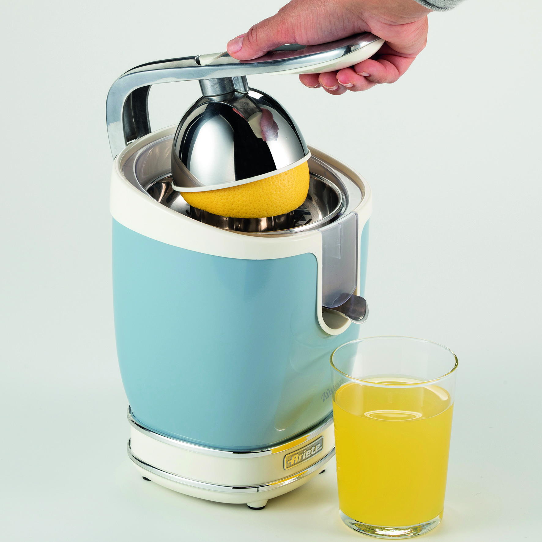 Una exprimidora de cítricos azul y blanca con un limón. Un vaso lleno.