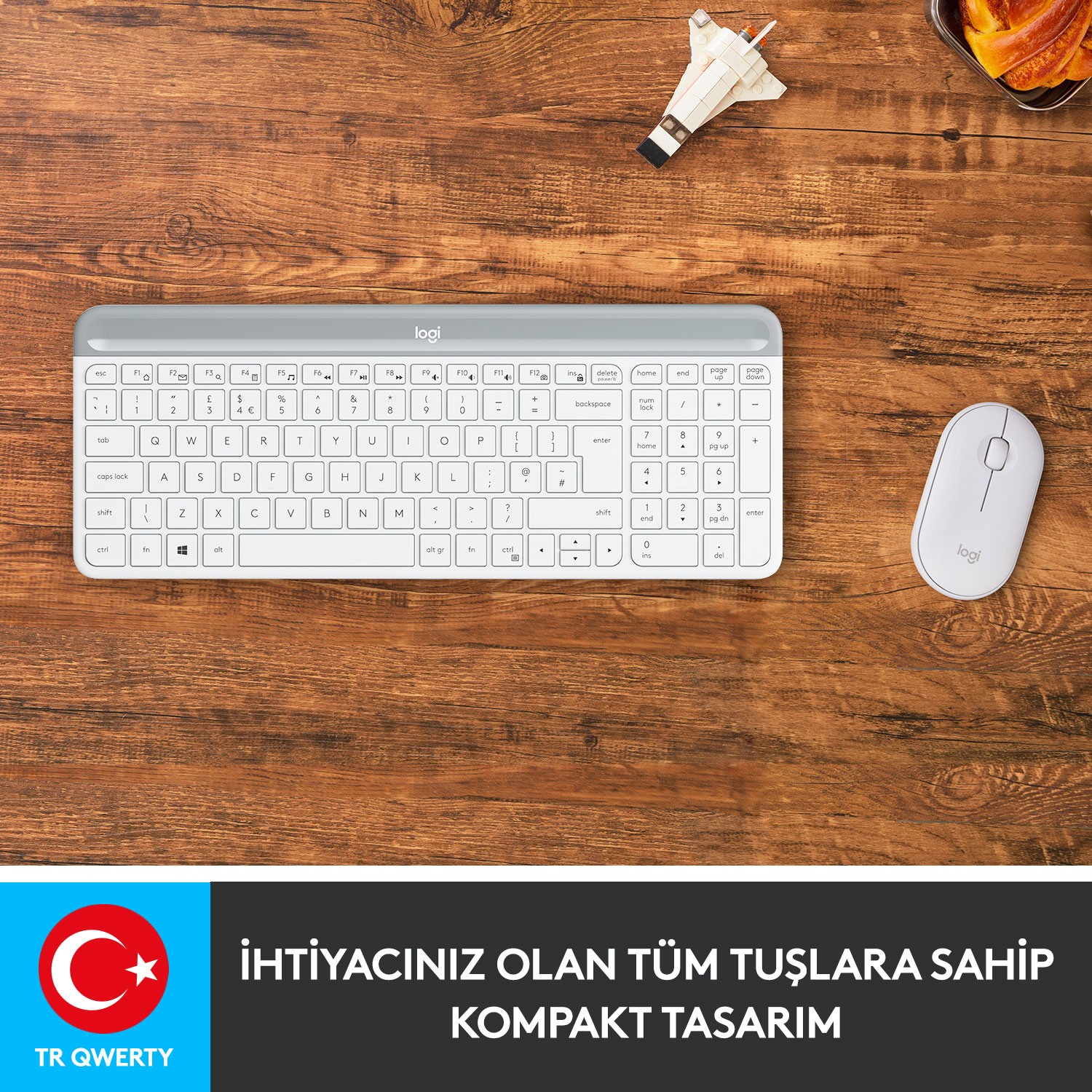 Beyaz bir klavye ve fare ahşap bir masanın üzerinde, bir oyuncak uçakla birlikte duruyor.