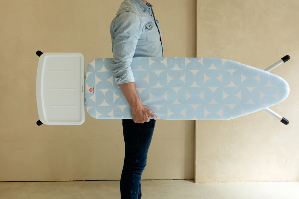 Une personne porte une planche à repasser à motifs bleus et blancs. La planche est pliée et tenue horizontalement.