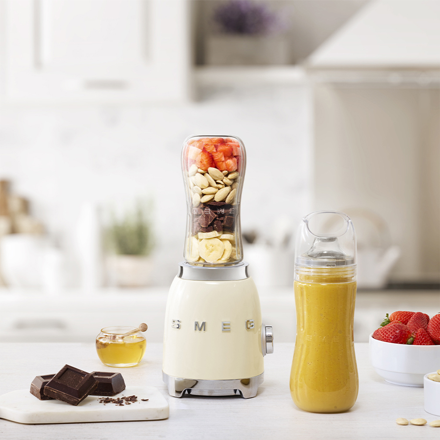 Frullatore Smeg con ingredienti all'interno. Sono presenti una ciotola di fragole, miele e cioccolato.