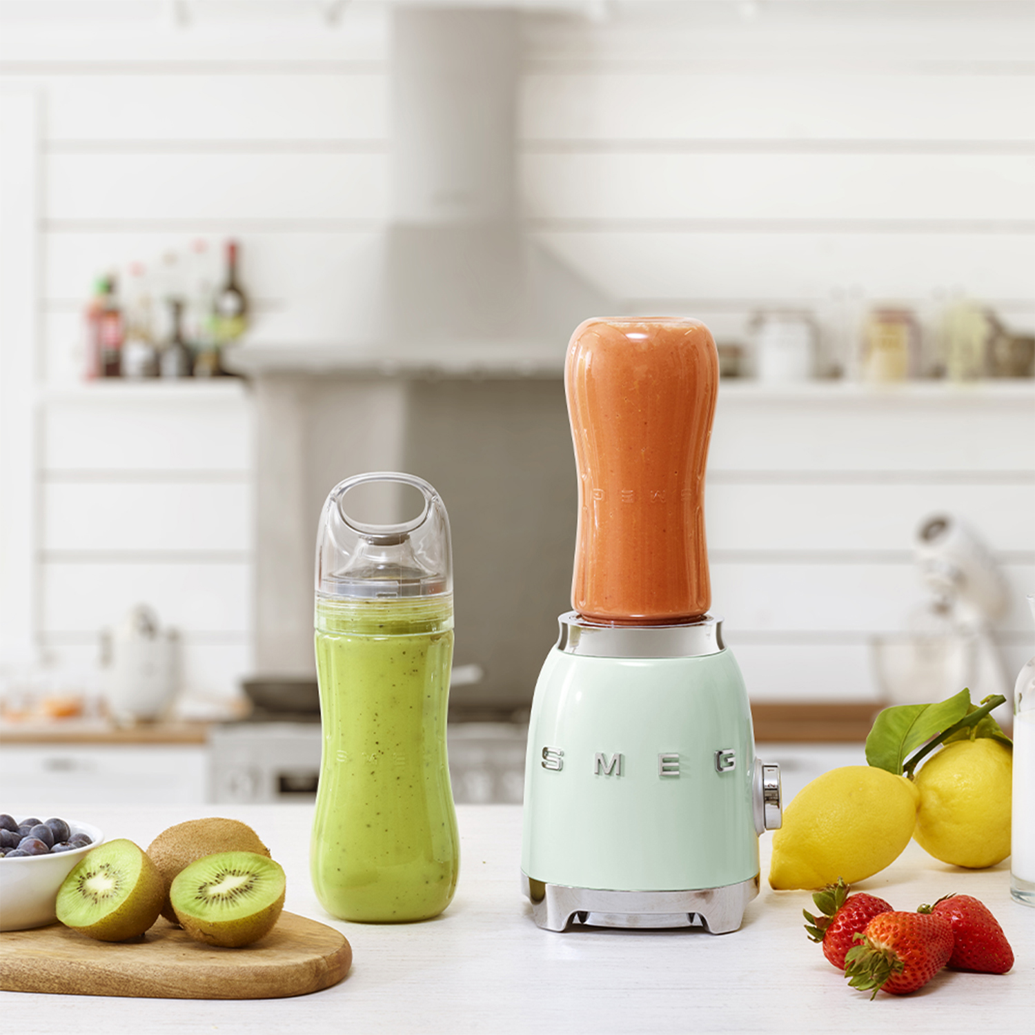 Un frullatore con uno smoothie, uno smoothie verde in bottiglia, kiwi, limoni e frutta.