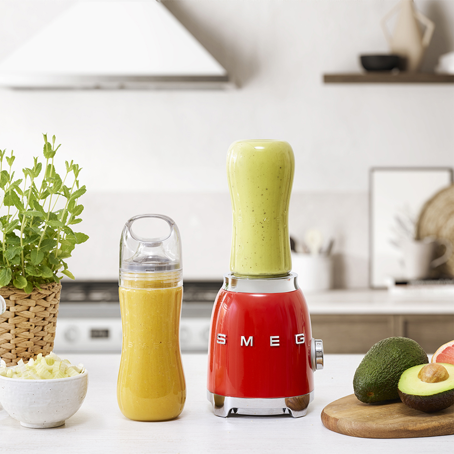 Un frullatore rosso con un frullato verde e una bottiglia di succo, circondato da cibo.