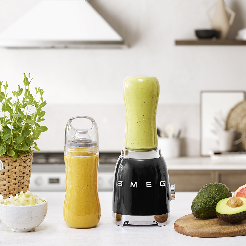 Un frullatore nero con un frullato verde e una bottiglia di succo, circondato da cibo.