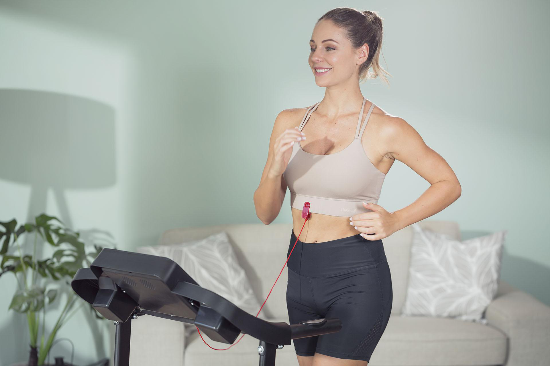 Frau läuft auf einem Laufband, trägt einen Sport-BH, in häuslicher Umgebung.