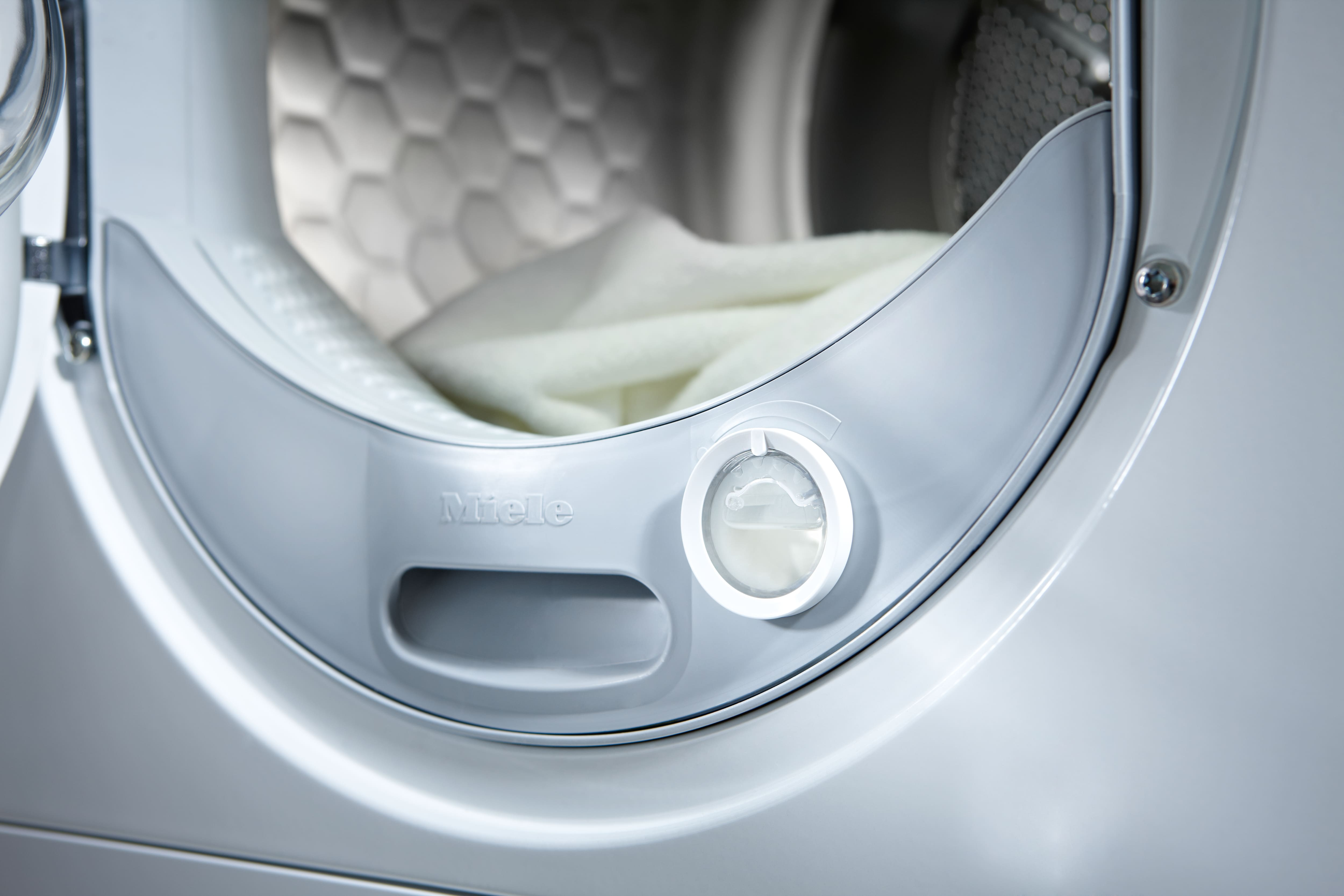 Innenansicht einer Miele Waschmaschine mit weißer Wäsche und einem Bedienelement.