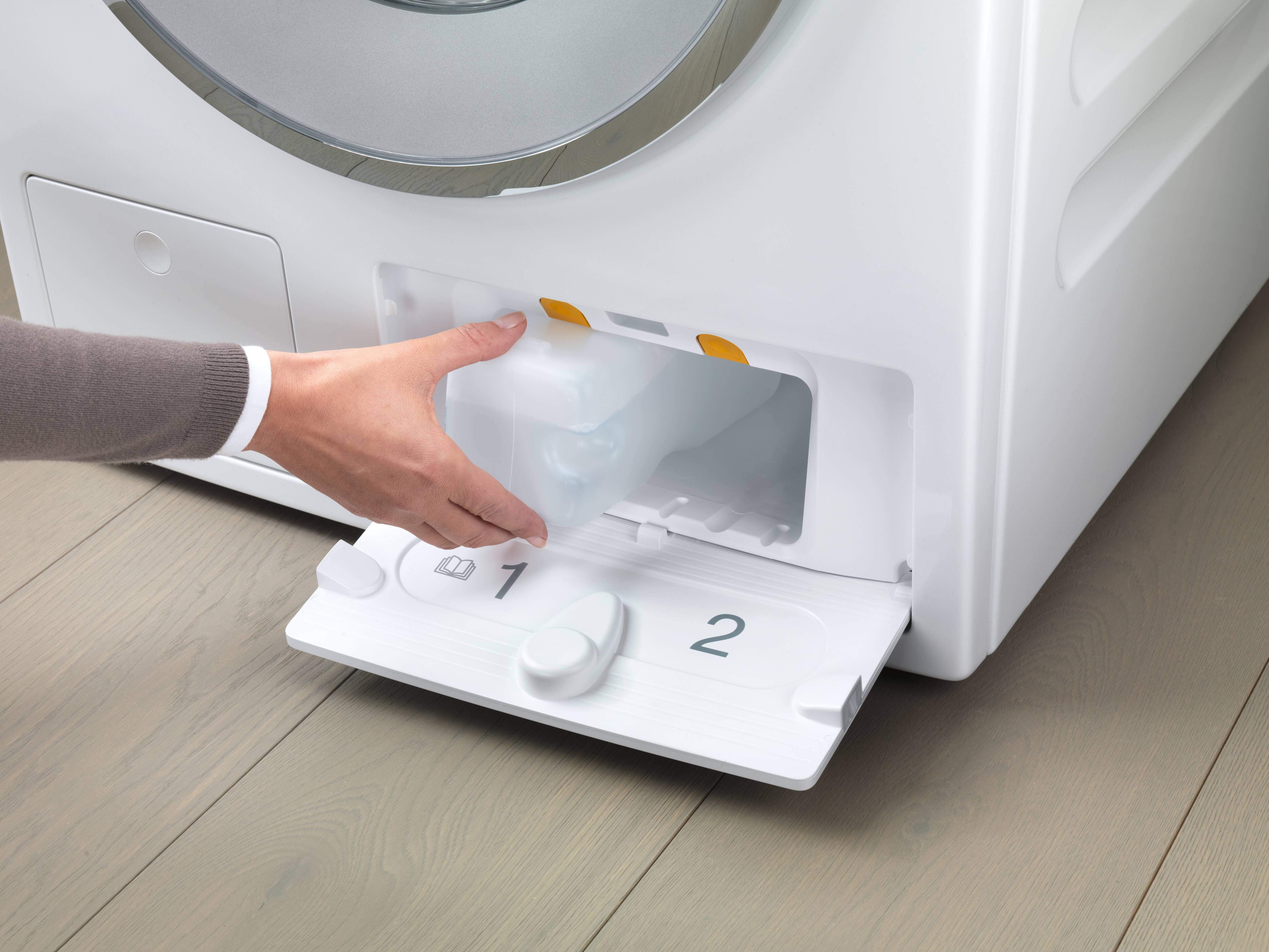 Die Hand einer Person entnimmt einen Behälter aus der Waschmittelkammer der Waschmaschine.