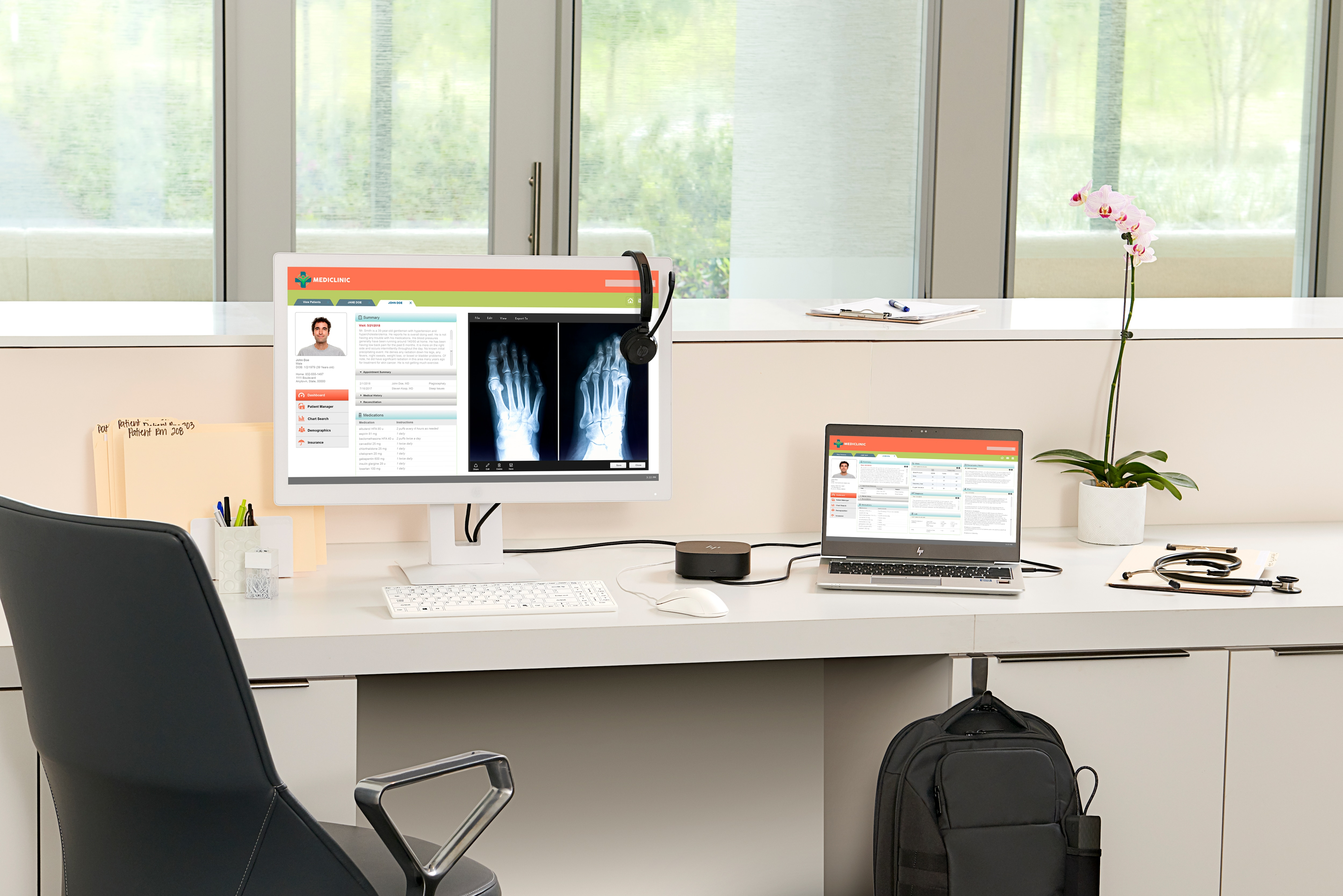 Büroschreibtisch-Setup mit Monitor, Laptop, Hub und Kopfhörern. Weißer Schreibtisch, Blume rechts.