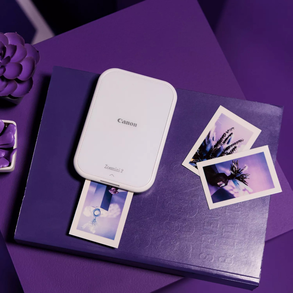 White Canon Zoemini 2 printer, purple background, with printed photos.