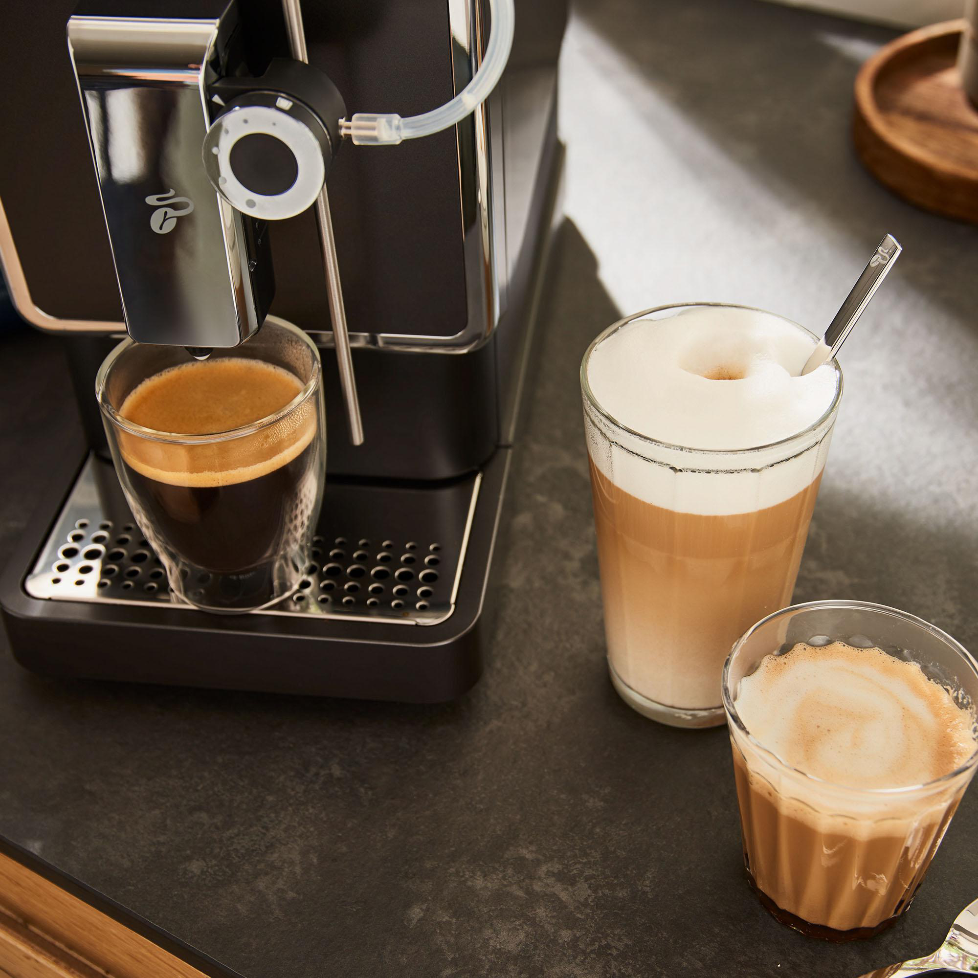 Espressomaschine mit zwei Kaffeegläsern. Ein Latte und ein Espresso. Schwarze Arbeitsplatte.