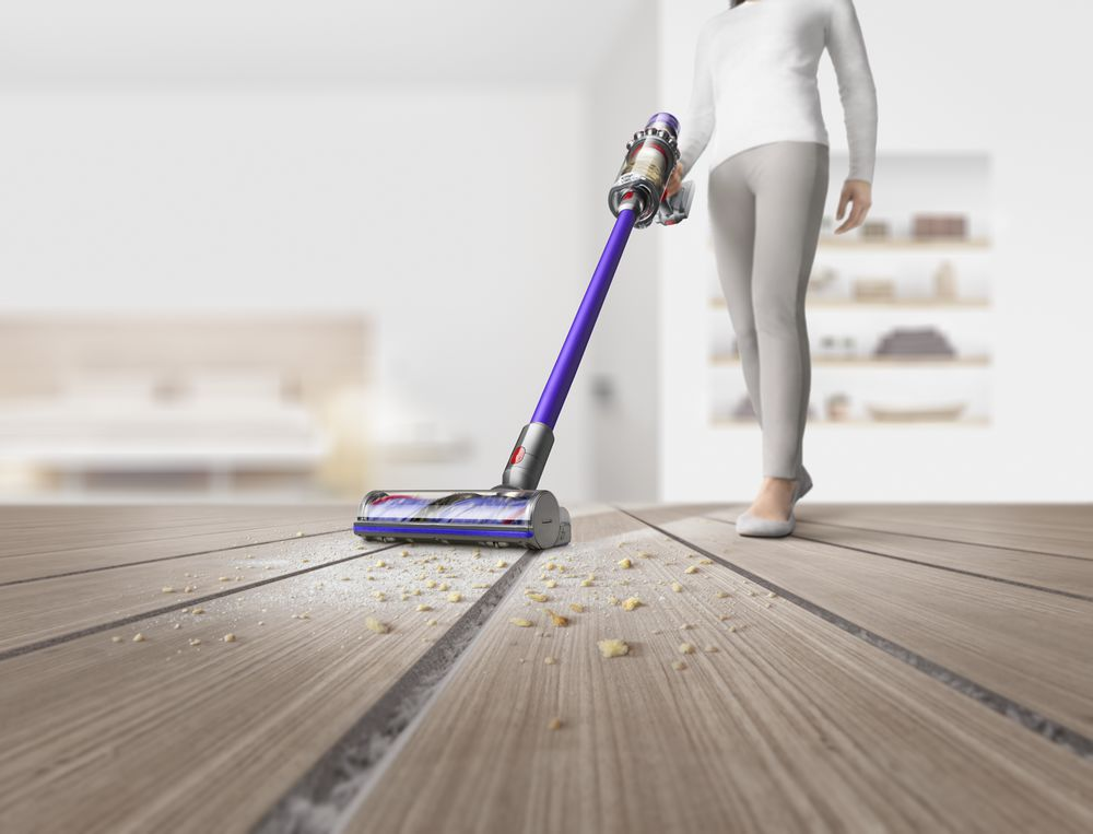 A person vacuums a wooden floor. Dust and crumbs are on the floor.