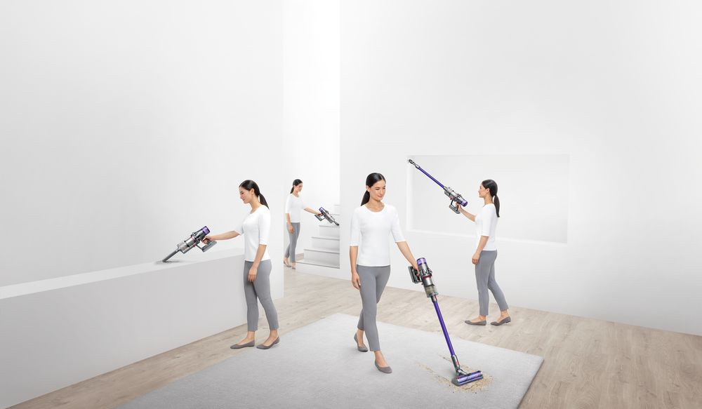 Woman using a Dyson vacuum cleaner in different positions. White walls, grey rug, and wooden floor.