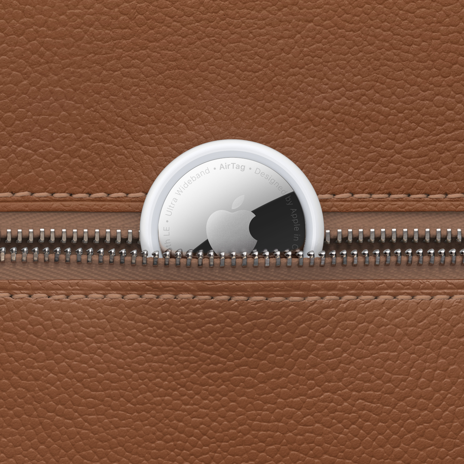 An Apple AirTag, white with the Apple logo, inside a brown leather zipper pocket.