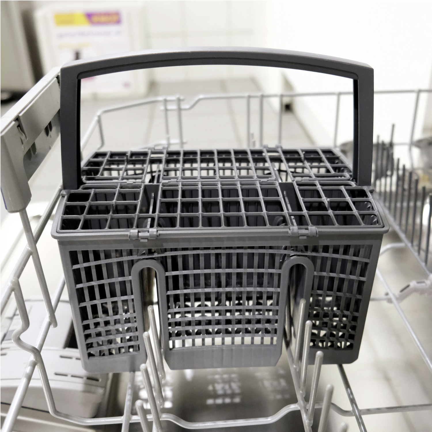Close-up of a gray dishwasher utensil basket inside a dishwasher. The basket is empty and ready to use.