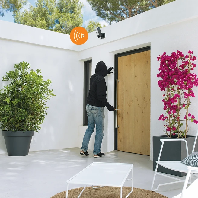 Personne en sweat à capuche noir essayant d'ouvrir une porte, avec lumière et plante.