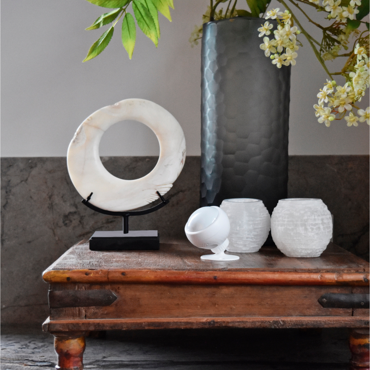 Een houten tafel met decoratieve objecten: een witte cirkel, een vaas en twee witte kandelaars.
