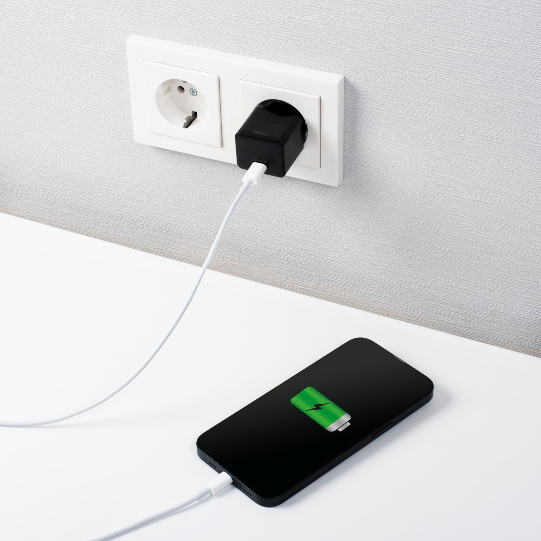 Image d'un téléphone en charge. Téléphone sur une table blanche connecté à un chargeur branché au mur.