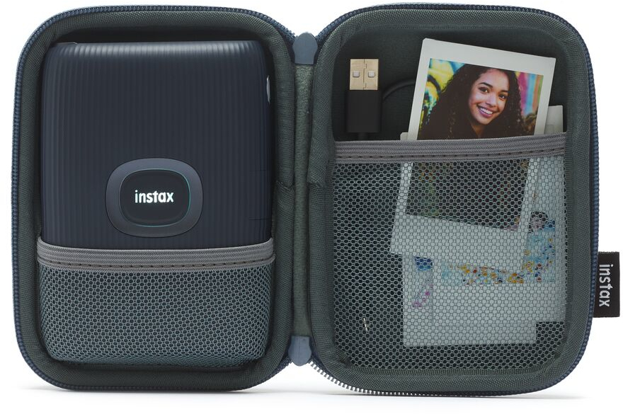 An open instax camera case with a camera, a cable, and a photo.