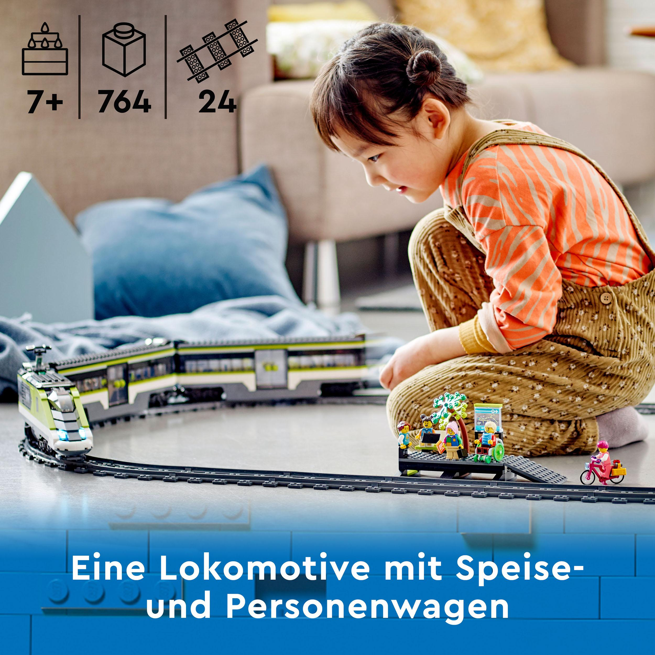 Ein Mädchen betrachtet ein Lego-Zug-Set mit Zug, Gleis und Figuren. Das Set steht auf blauer Oberfläche.