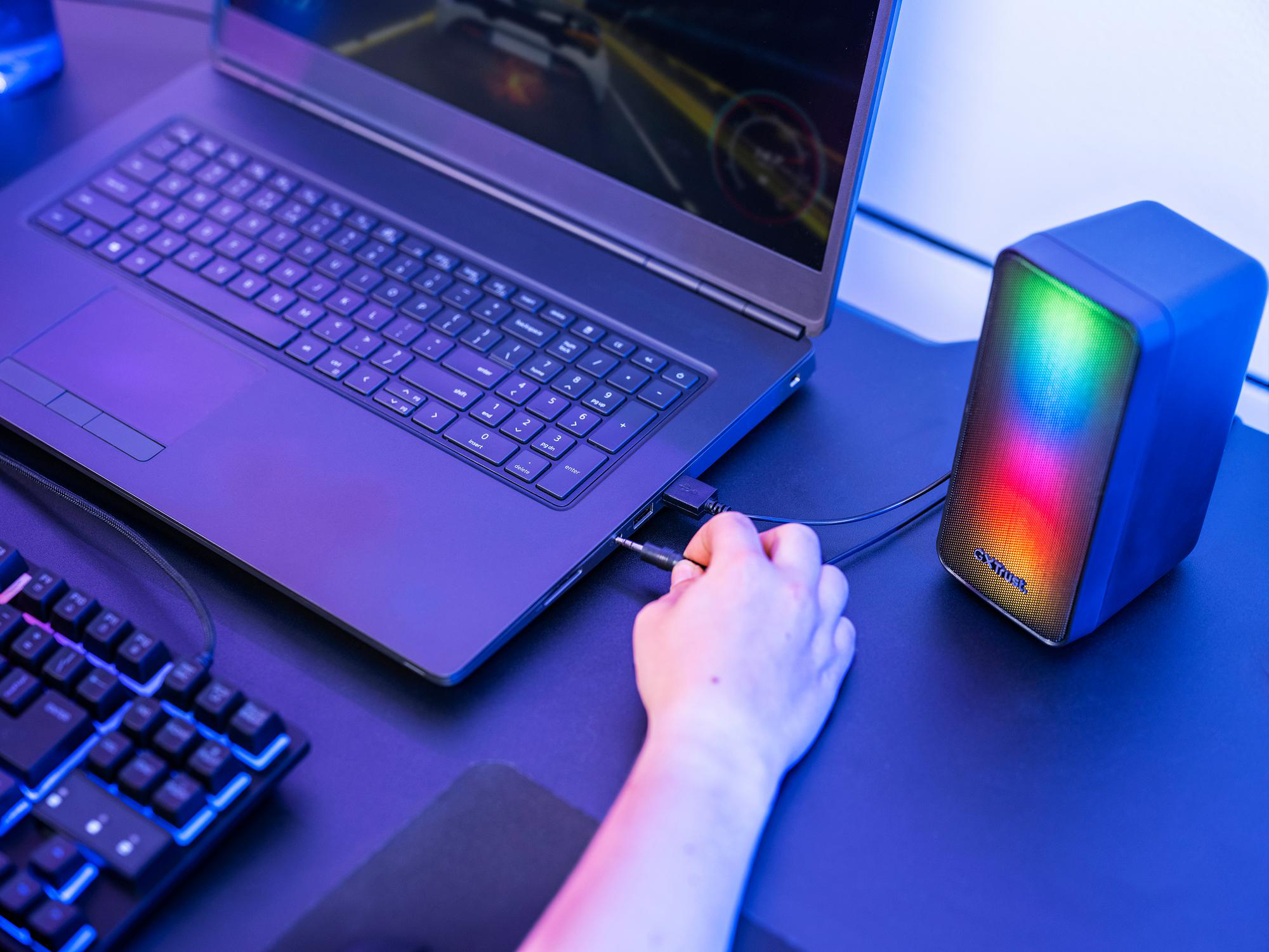 Hand verbindet Audiokabel mit Laptop neben beleuchtetem Lautsprecher.