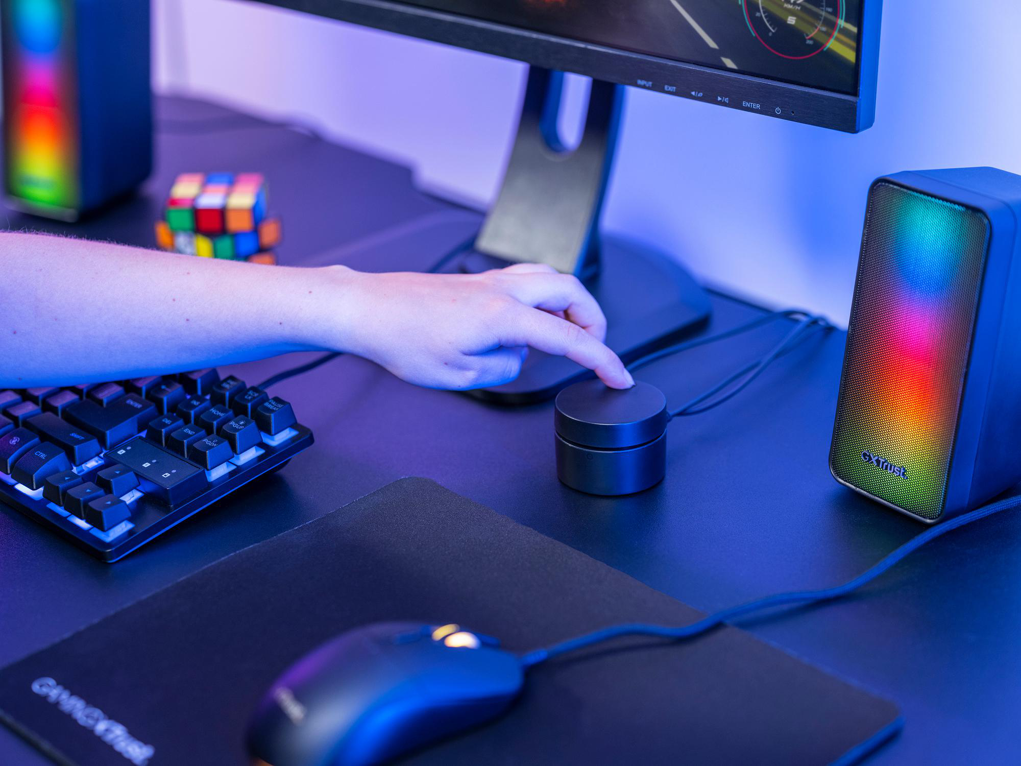Hand drückt runden Regler auf Gaming-Schreibtisch neben Tastatur und beleuchtetem Lautsprecher.