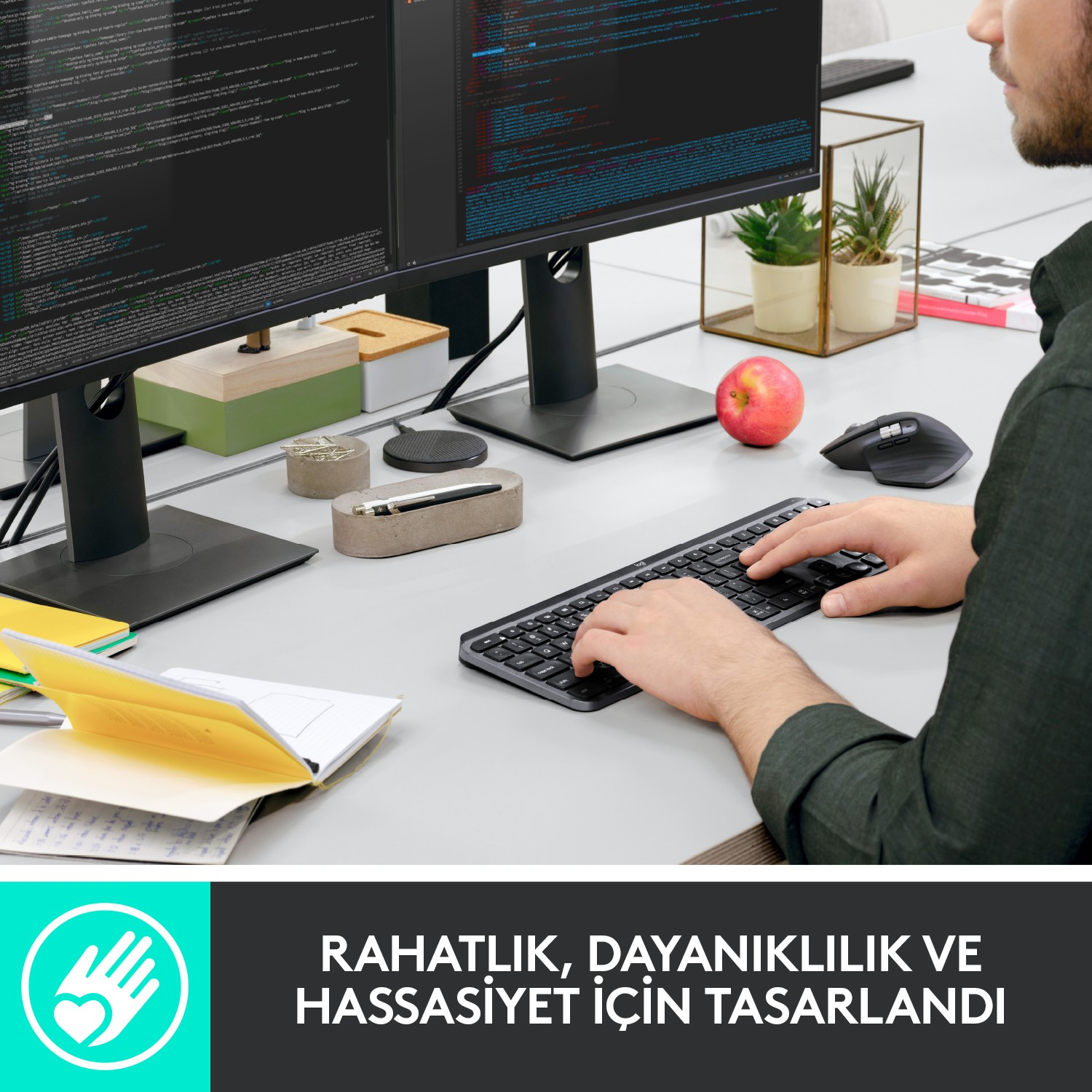 Bir kişi, bir masada iki monitör, klavye ve fare ile bilgisayarda çalışıyor.