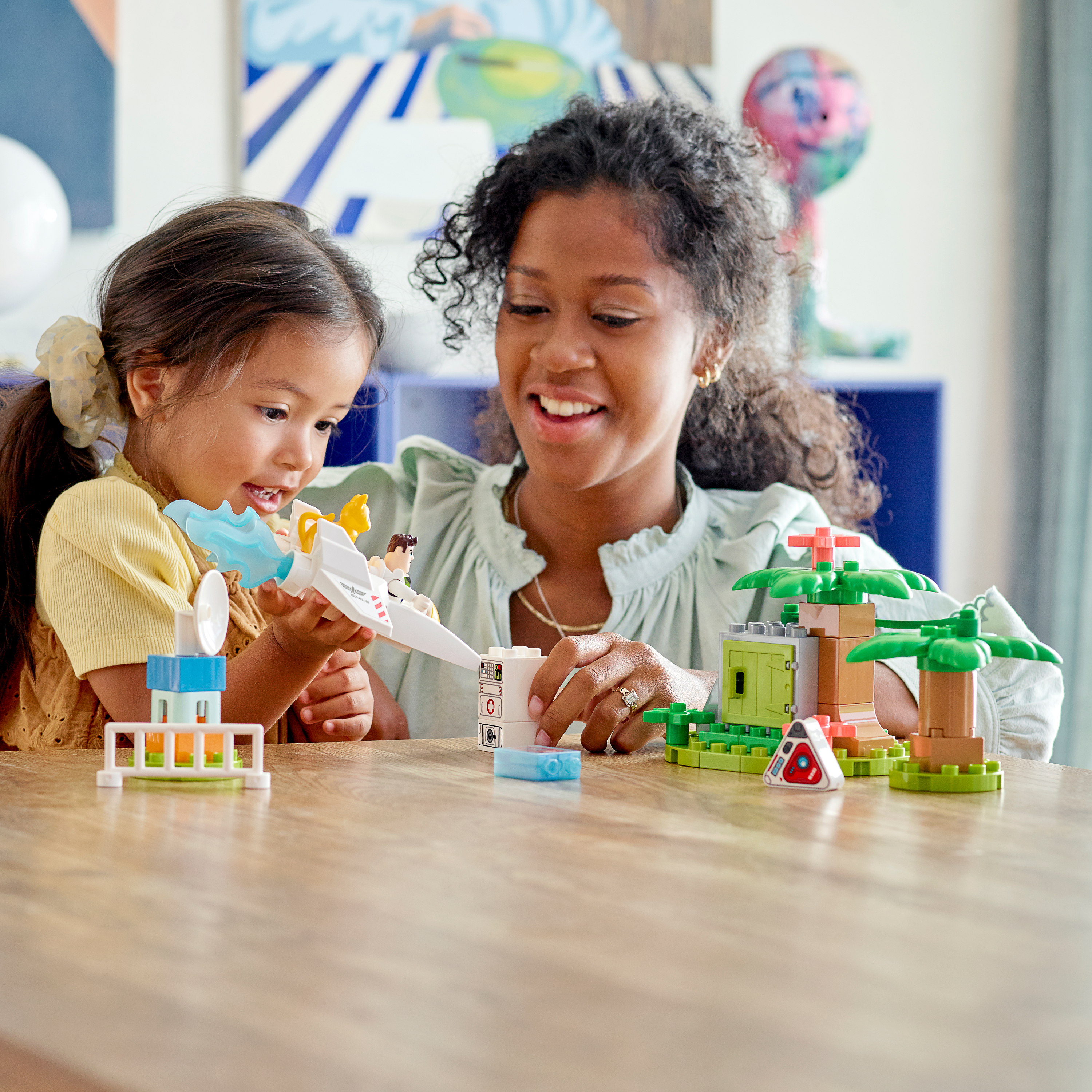 Eine Frau und ein Mädchen spielen mit Duplo-Bausteinen, bauen ein Spielzeugflugzeug und ein Gebäude.