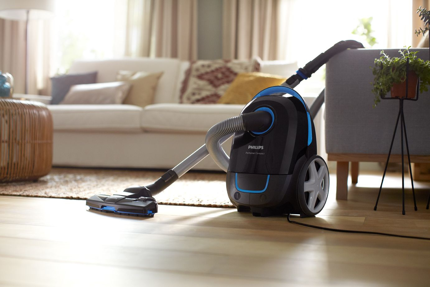Ein schwarz-blauer Philips Staubsauger auf Holzboden. Im Hintergrund sind ein weißes Sofa und Dekorationen zu sehen.