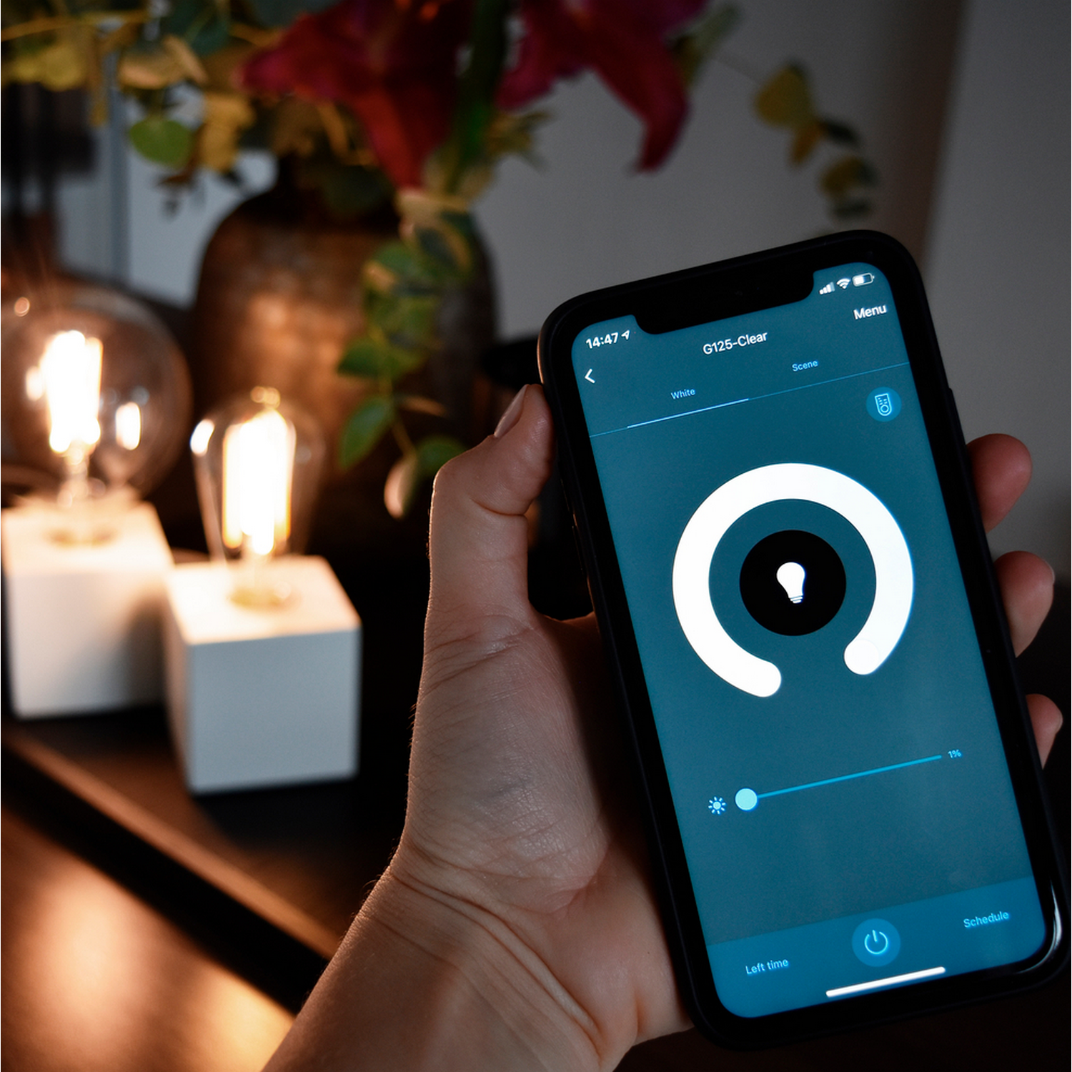 Een hand die een smartphone vasthoudt met een app voor slimme lampbediening. Twee brandende lampen op de achtergrond.
