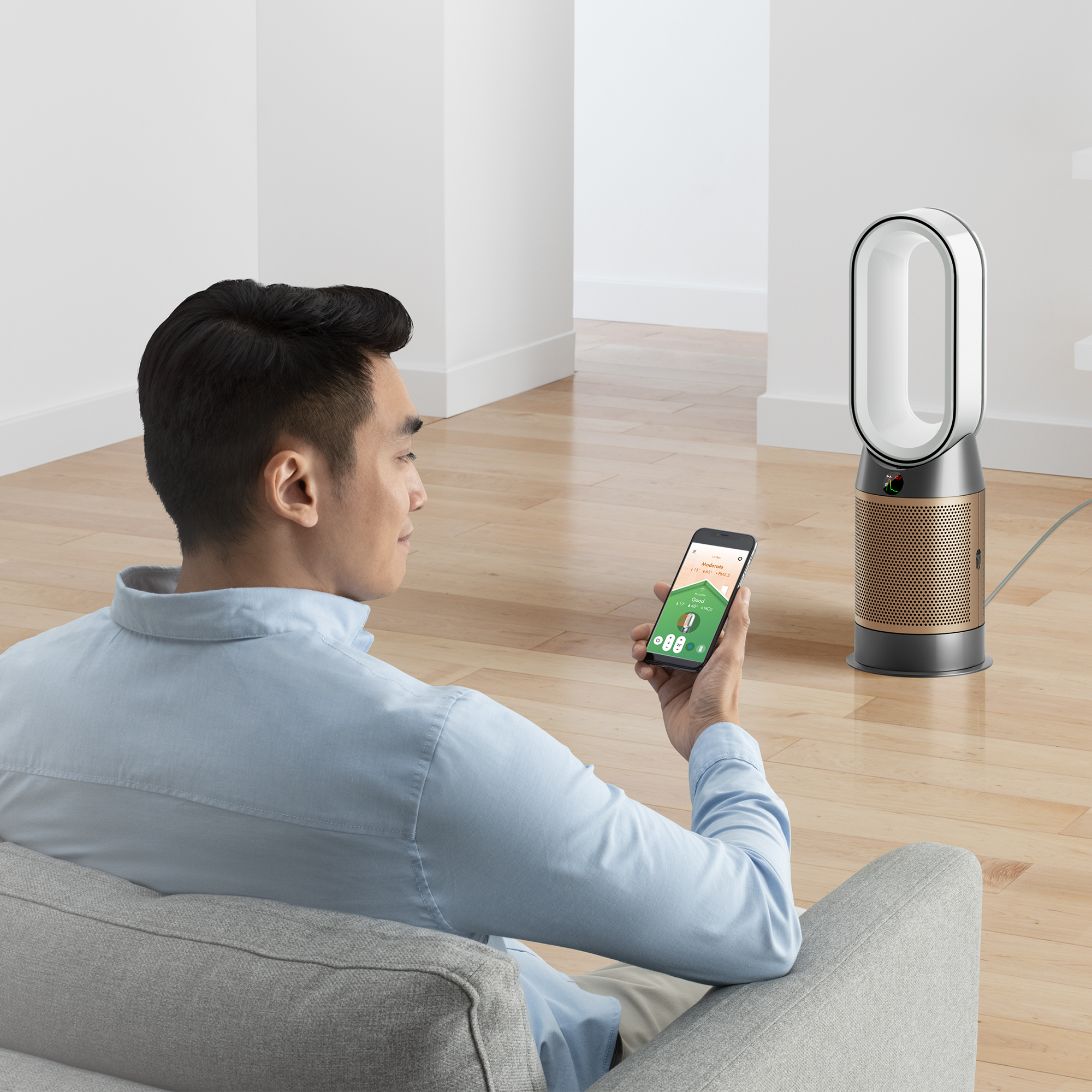 Un homme en chemise bleue utilise un smartphone devant un purificateur d'air blanc et doré.