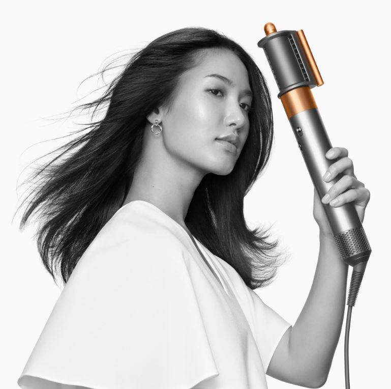 Donna che tiene in mano uno strumento per lo styling dei capelli. Guarda la fotocamera su sfondo bianco.