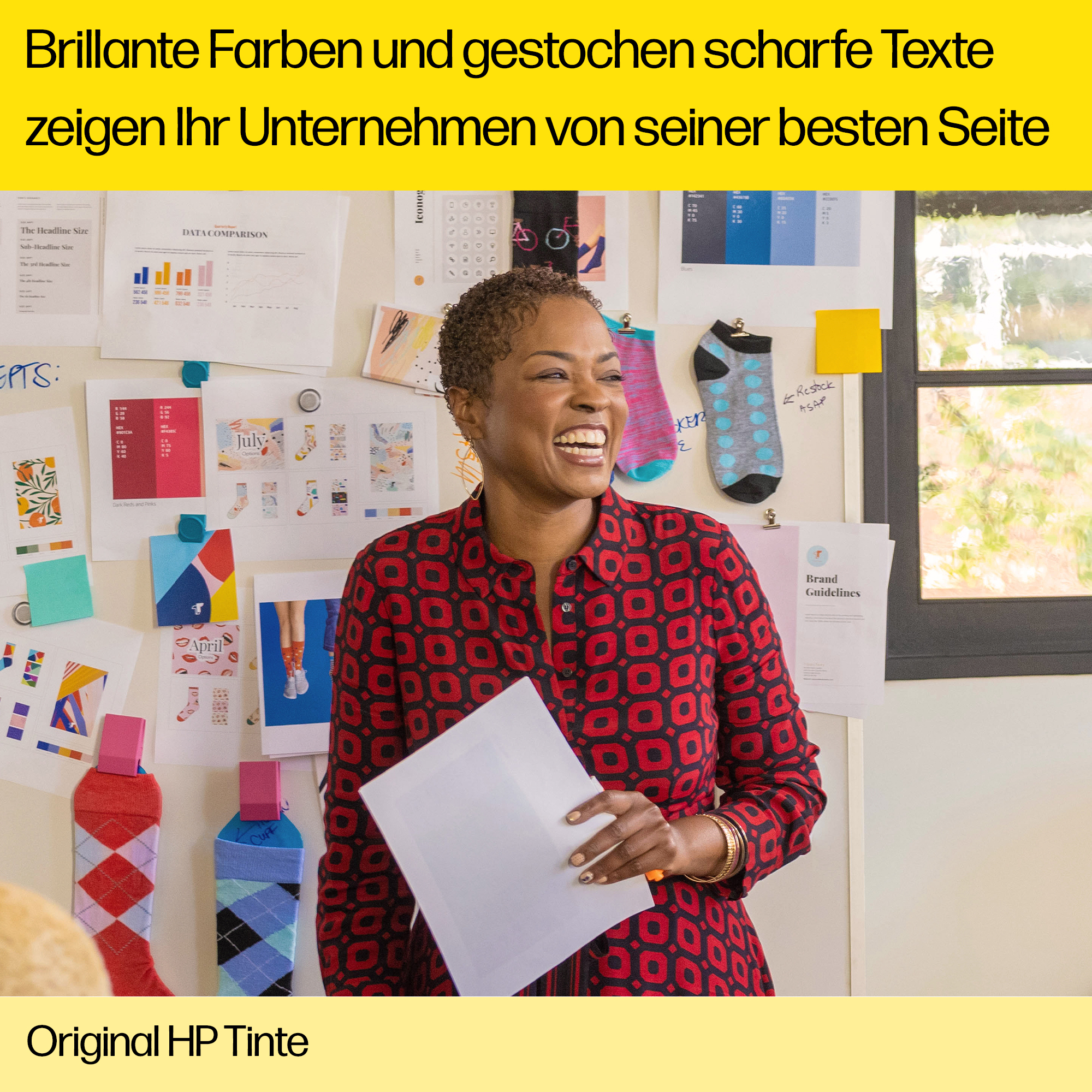 Frau lächelt, hält ein Papier. Eine Pinnwand ist hinter ihr mit Papieren und Socken, die daran befestigt sind.