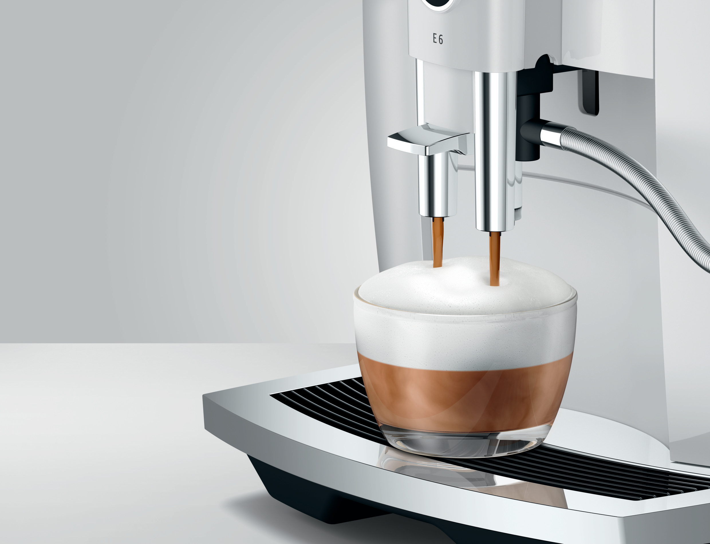 Kaffeemaschine gießt Kaffee in ein Glas mit Milchschaum.