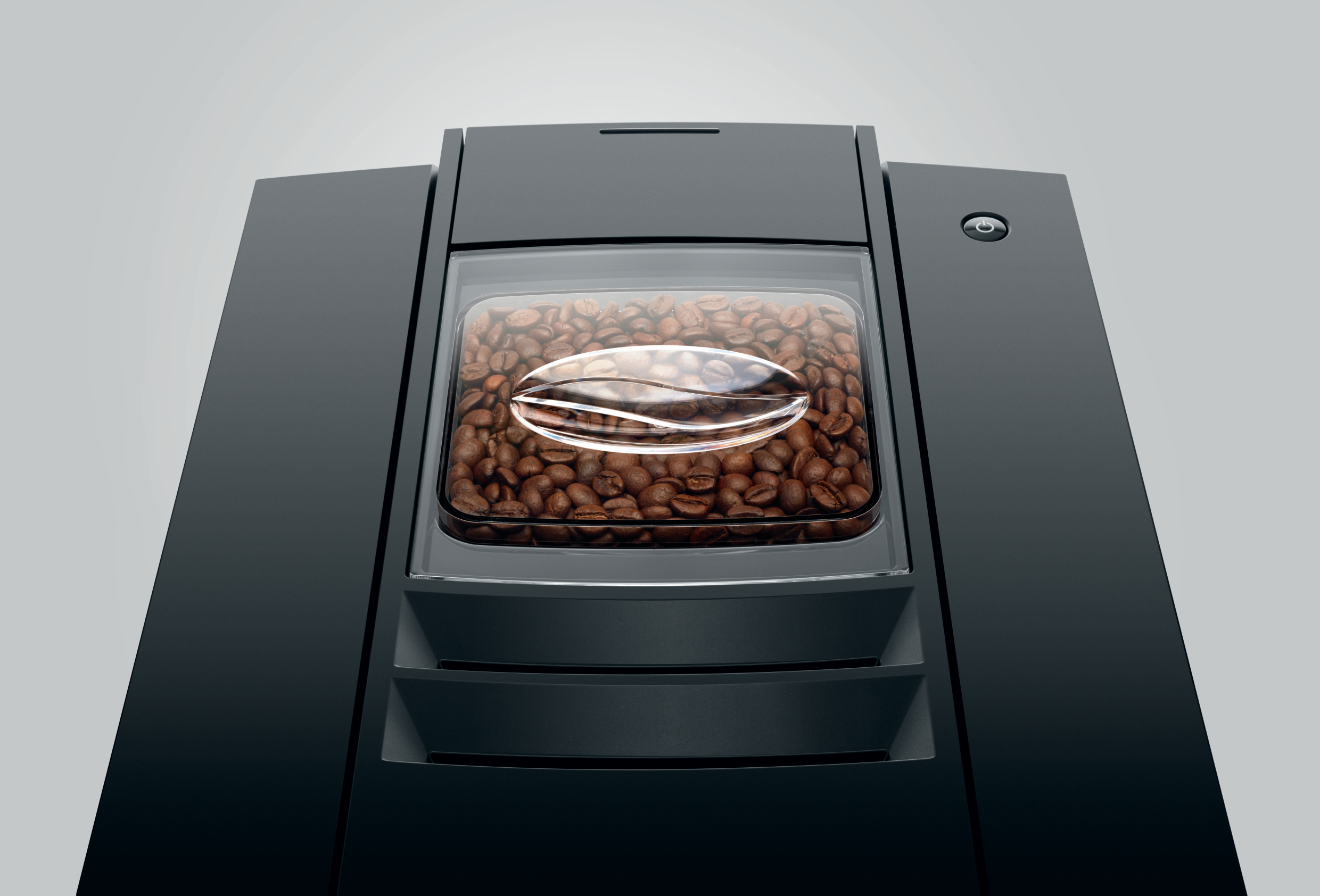 Bohnenbehälter einer schwarzen Kaffeemaschine mit braunen Kaffeebohnen.