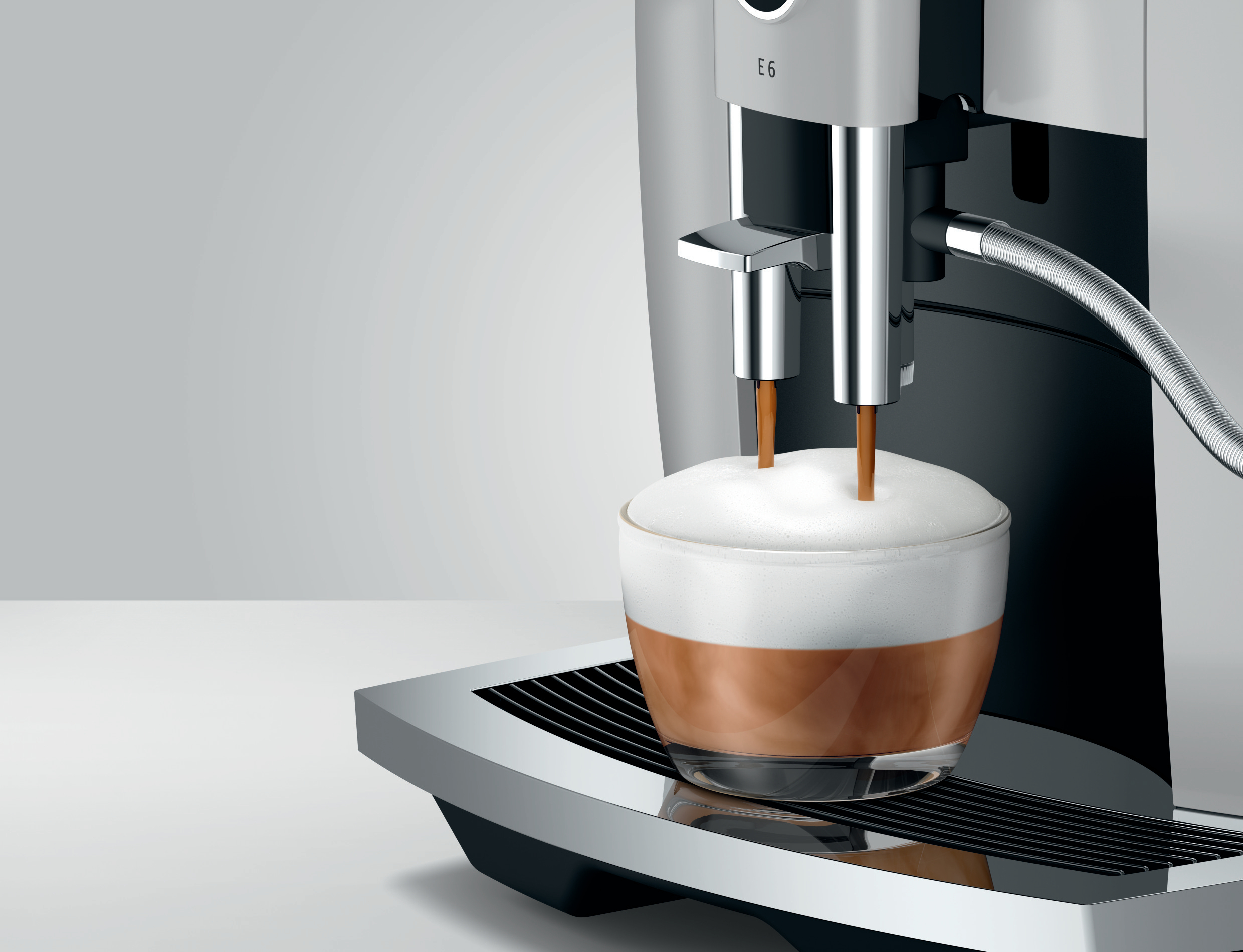 Kaffeemaschine, die Kaffee in ein Glas mit Schaum abgibt. Edelstahlgehäuse und schwarzer Sockel.