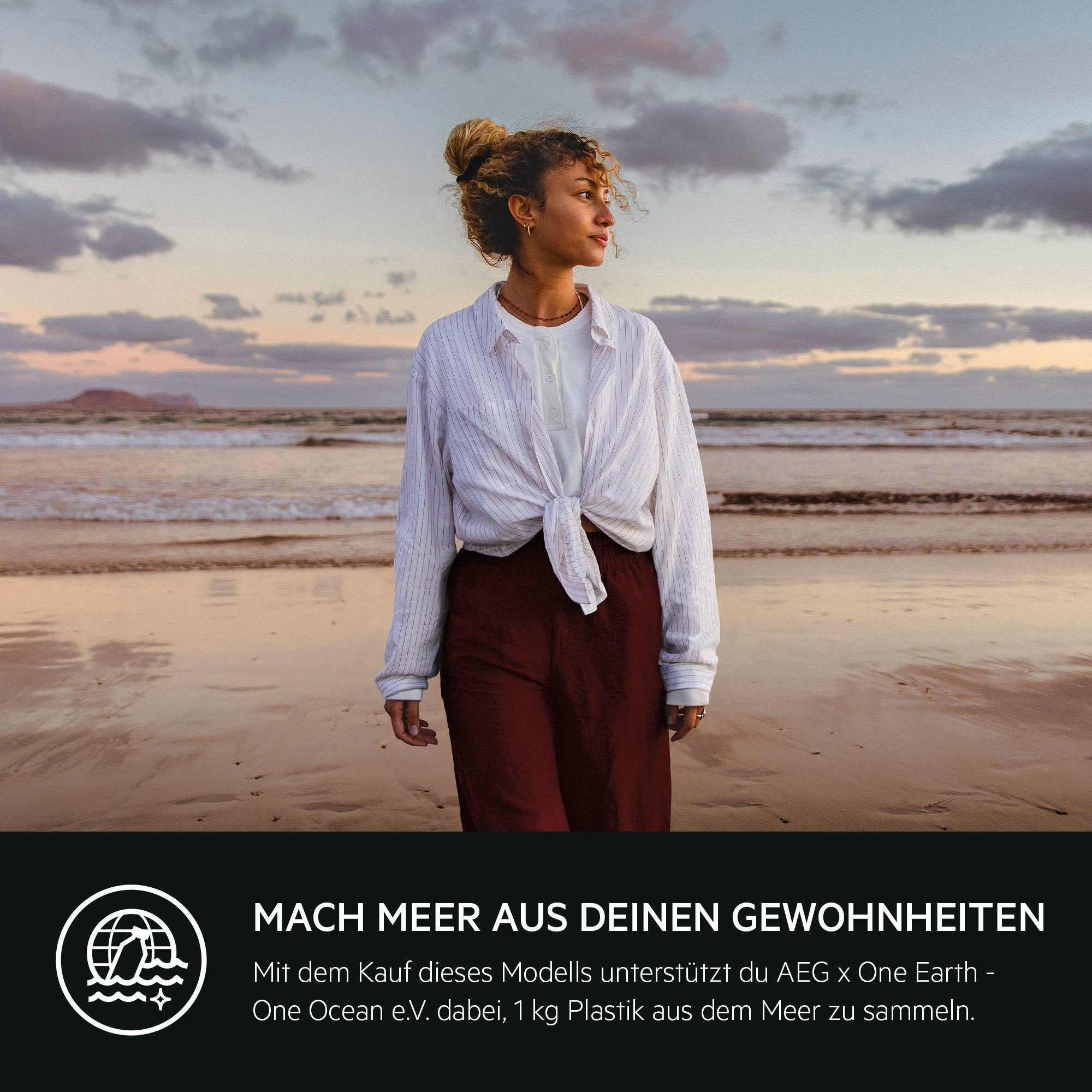 Eine Frau mit Dutt steht am Strand und blickt auf das Meer. Der Himmel ist bewölkt und die Sonne geht unter.