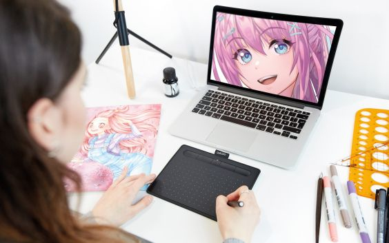 Une femme dessine sur une tablette connectée à un ordinateur portable affichant de l'art animé. Fournitures de dessin.
