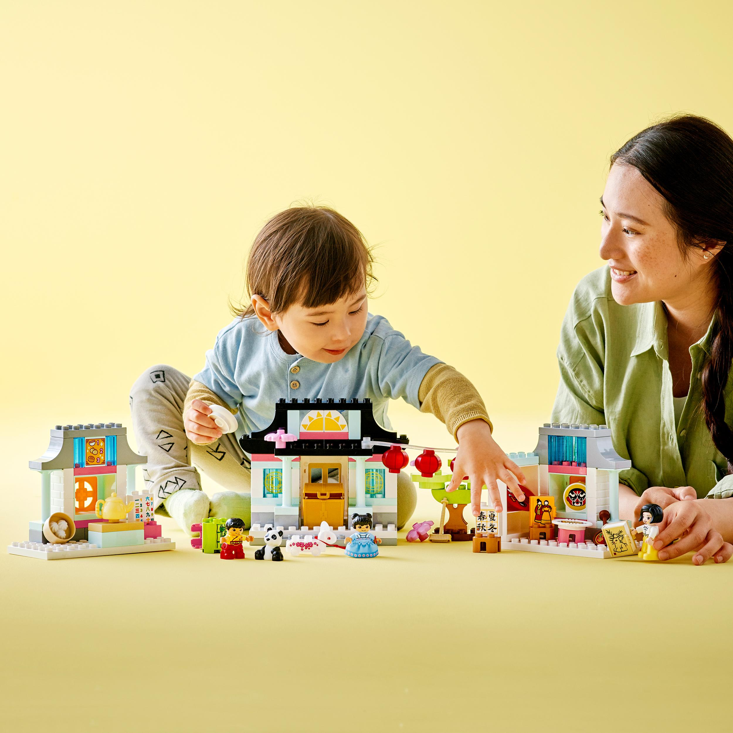 Ein Kind und ein Erwachsener spielen mit LEGO-Spielzeug. Mehrere LEGO-Strukturen und Figuren sind sichtbar.