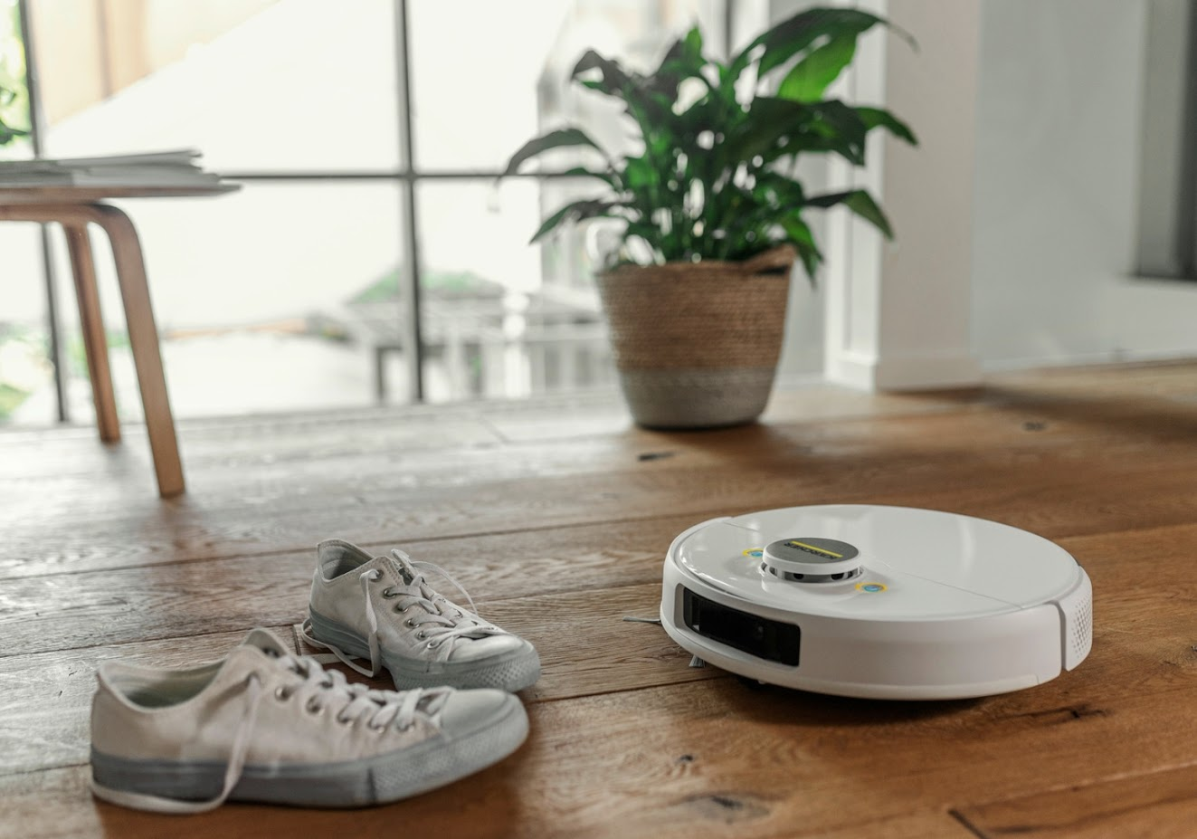 Spor ayakkabı ve bir bitkiyle ahşap zeminde robot süpürge.