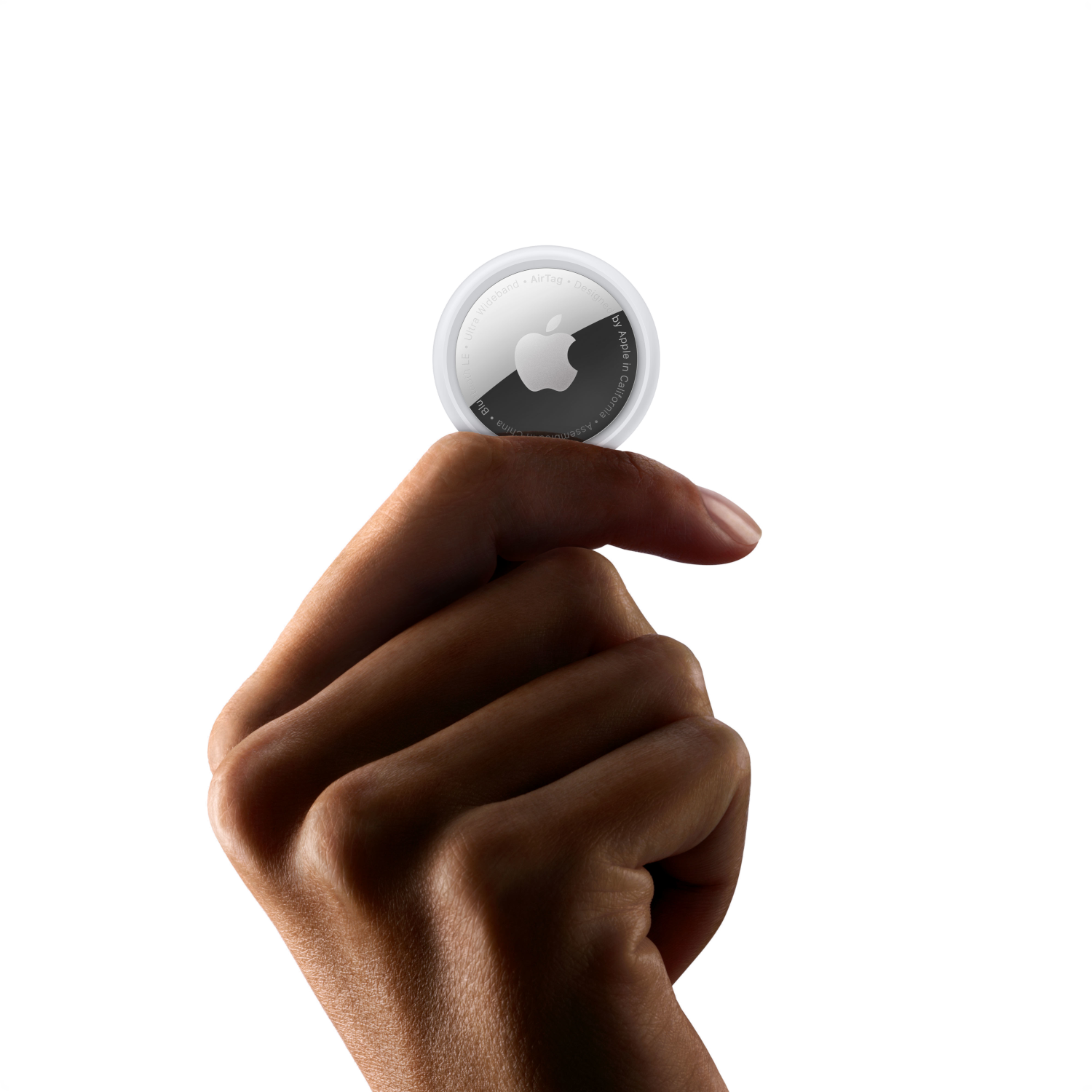 Hand holding a white Apple AirTag, with the Apple logo facing the camera, against a black background.