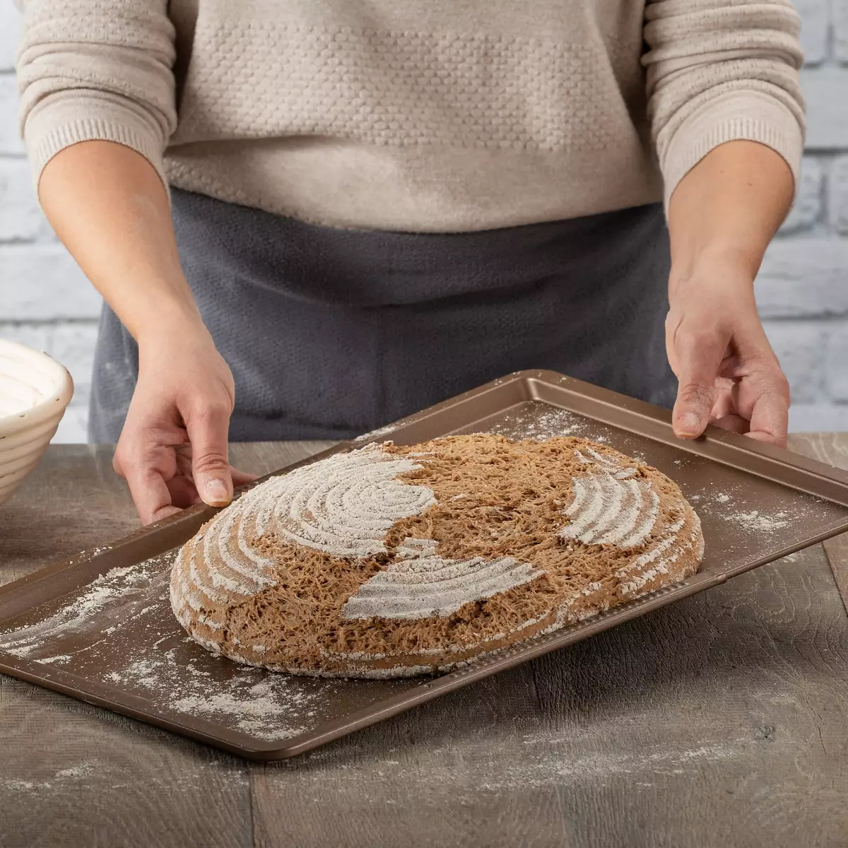 Eine Person hält ein Backblech mit einem Brotlaib darauf und zeigt das Brot.