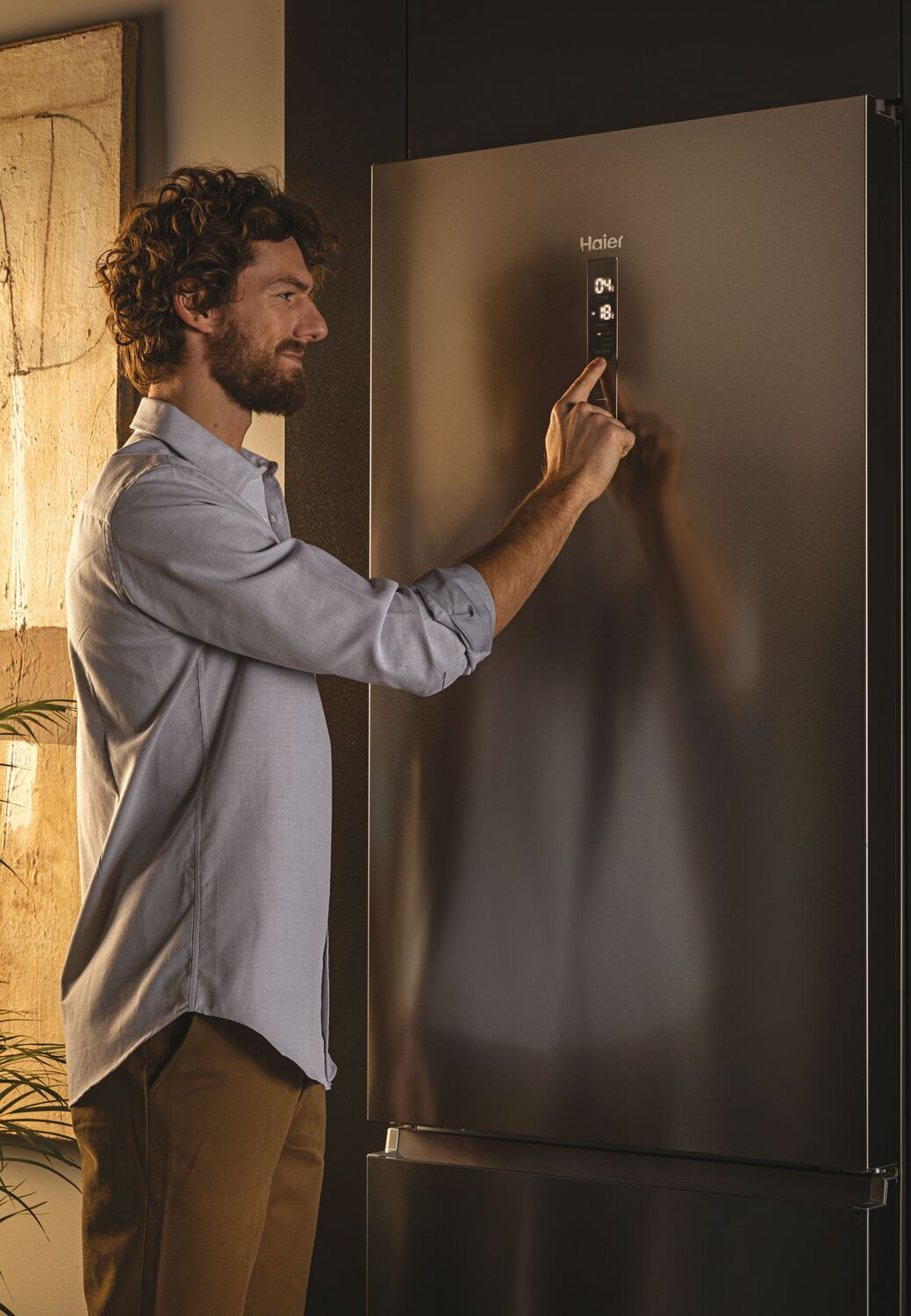 Hombre tocando panel de control de refrigerador Haier, con pantalla digital, en cocina moderna.