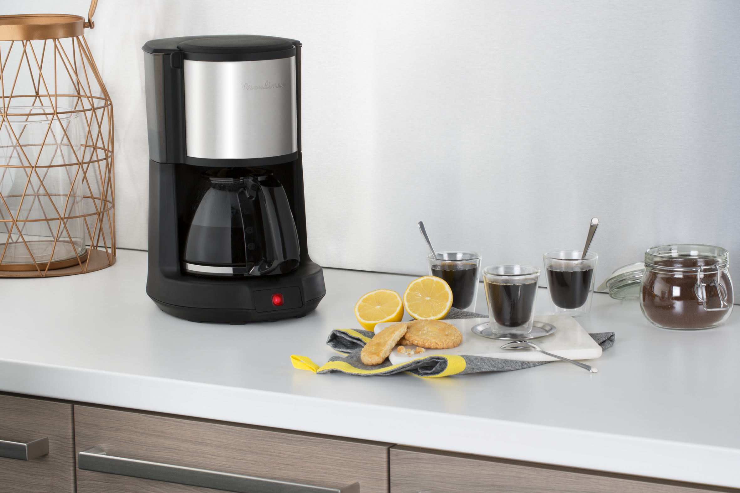 Una cafetera con accesorios: limones, galletas y tazas de café en una encimera blanca.