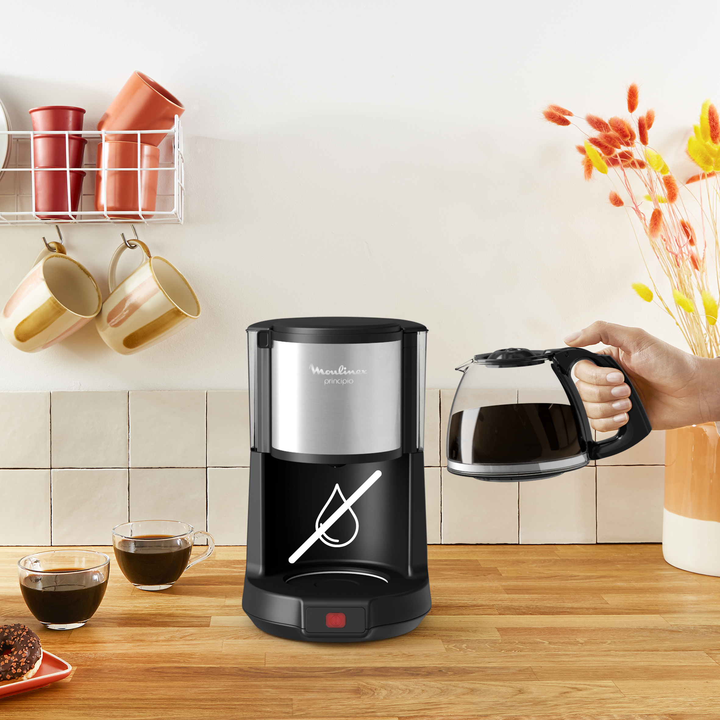 Cafetera negra con jarra de vidrio y tazas, sobre una superficie de madera.