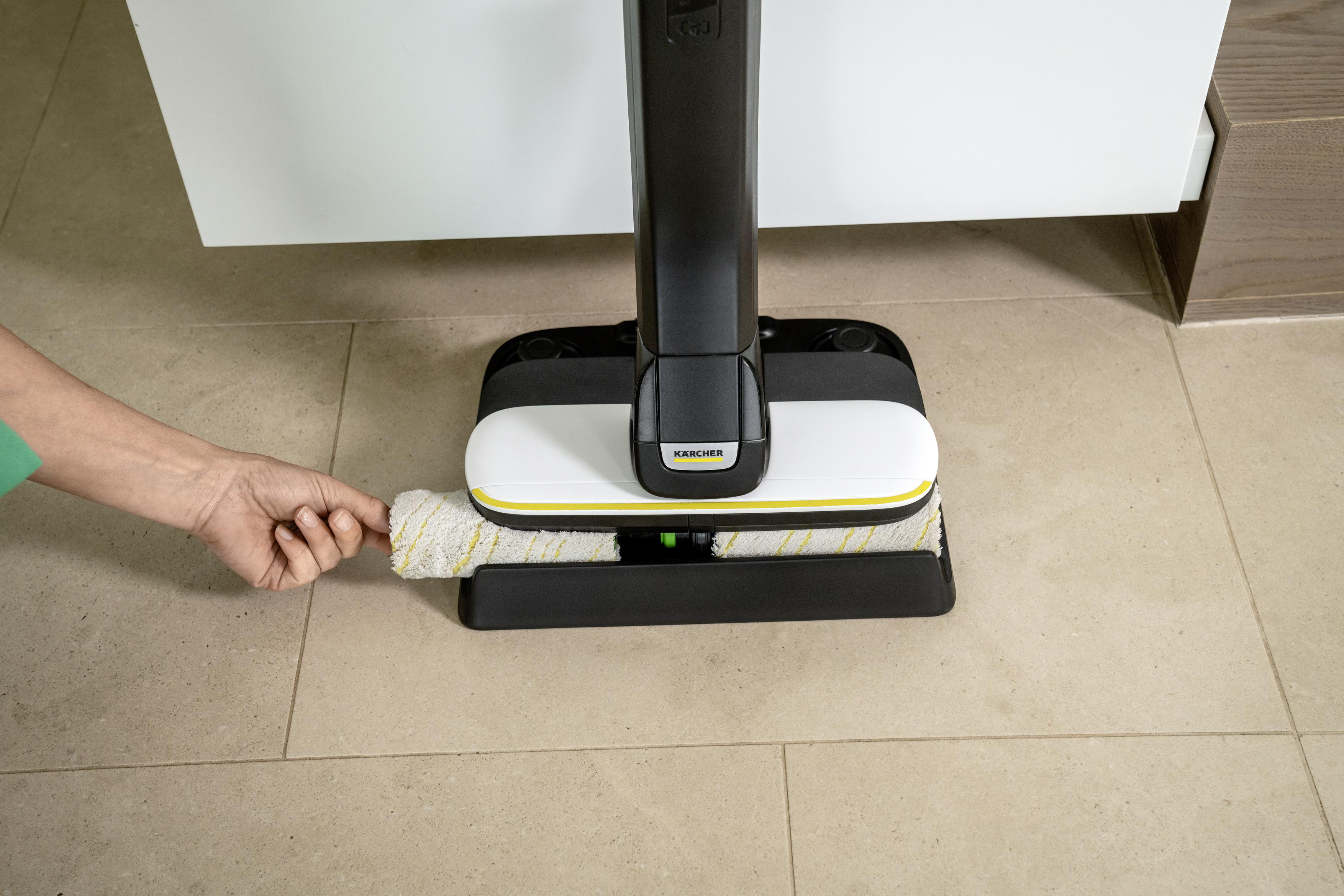 Eine weiß-gelbe Bodenreinigungsmaschine mit der Hand einer Person. Die Maschine steht auf einem gefliesten Boden.