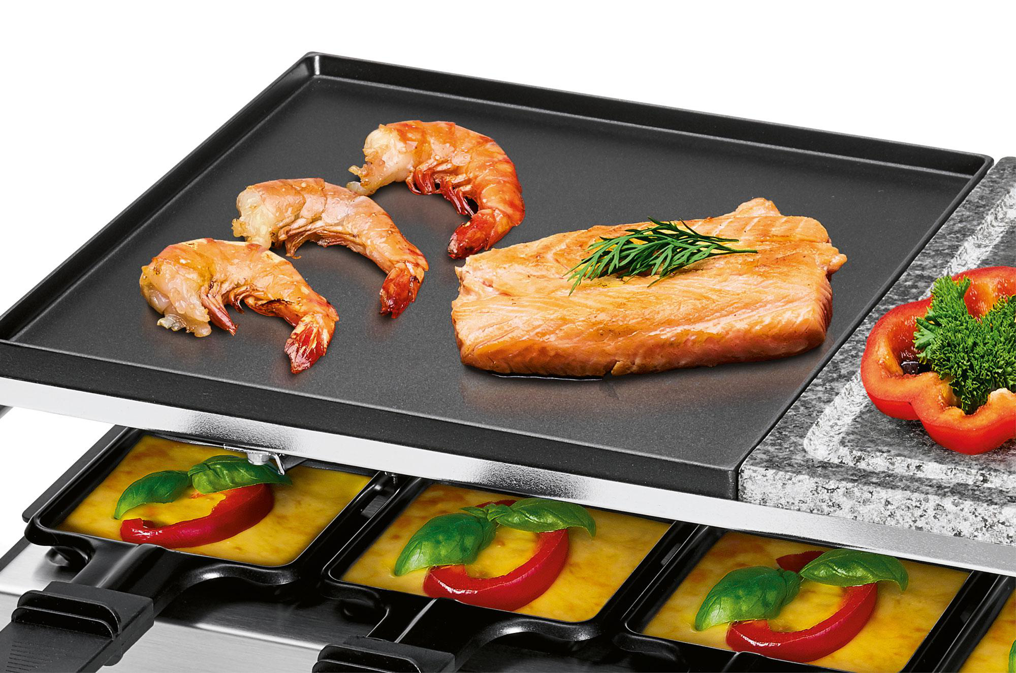 Ein Raclette-Grill mit Garnelen, Lachs und Gemüse oben. Käse und Paprika unten.