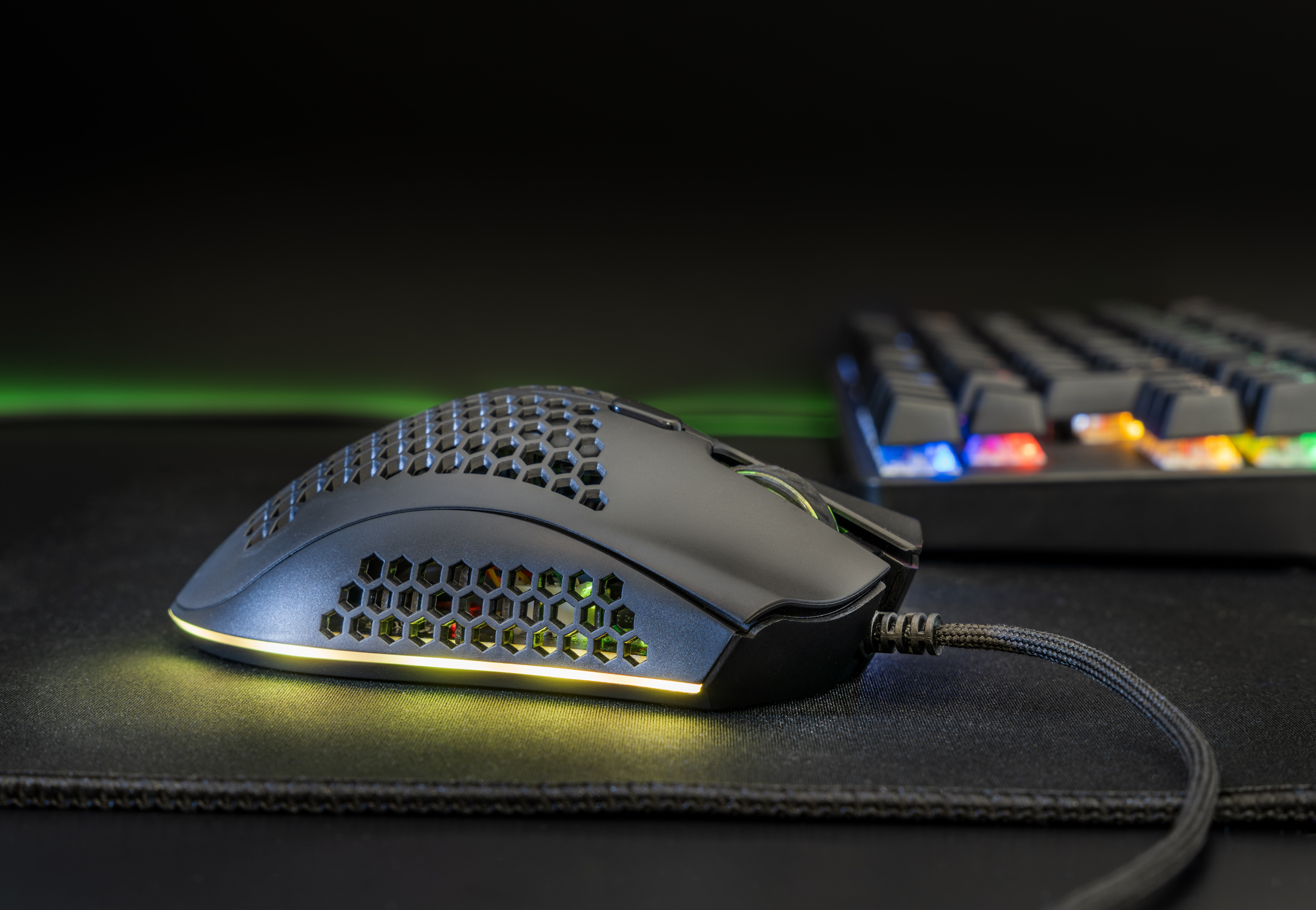 Un mouse da gioco nero con design a nido d'ape, tastiera sullo sfondo.