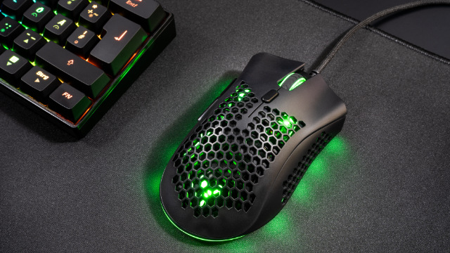 Un mouse da gioco nero con luci verdi è su un tappetino nero accanto a una tastiera.