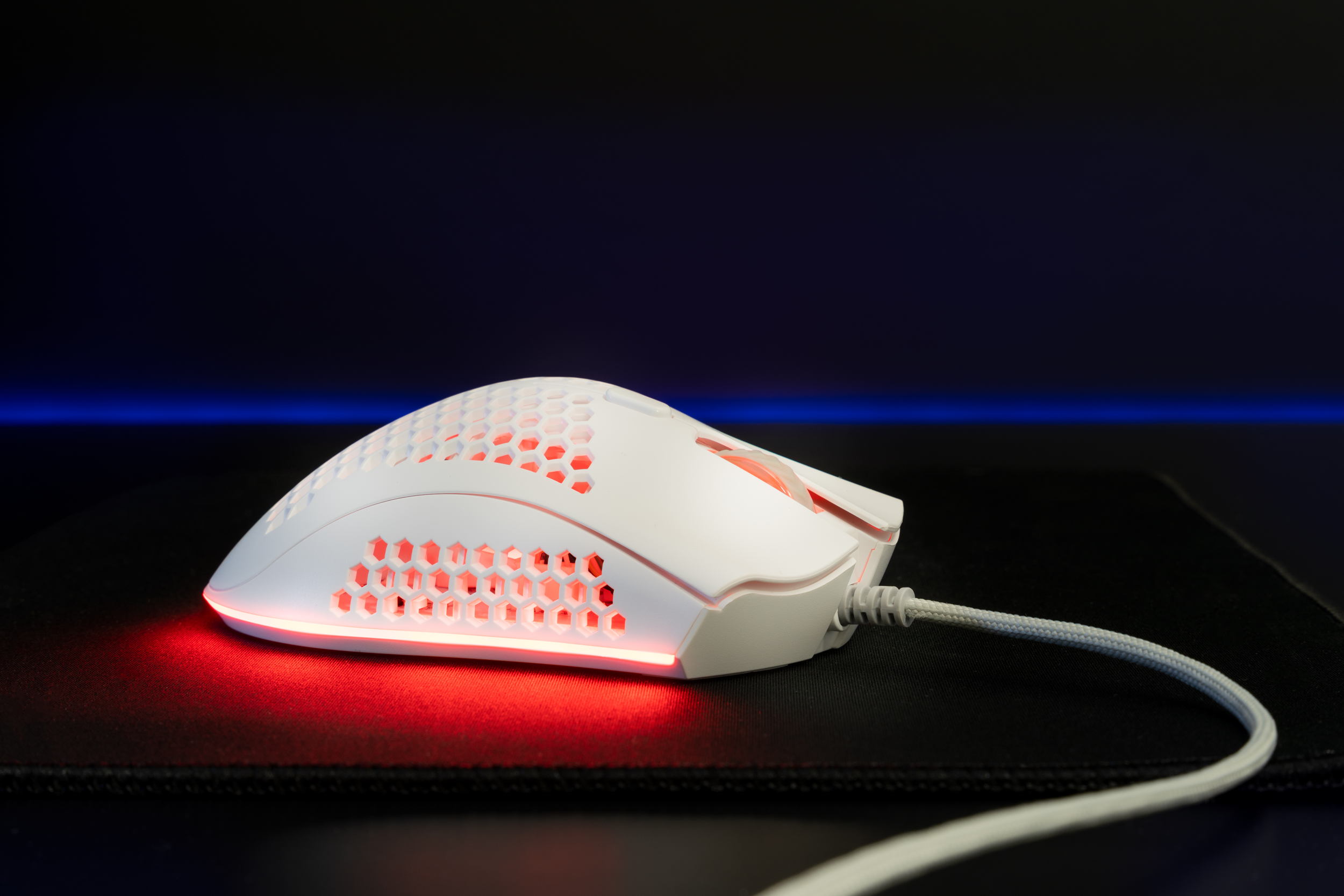Mouse da gioco bianco con design a nido d'ape e illuminazione a LED rossa, su un tappetino nero con luce blu.