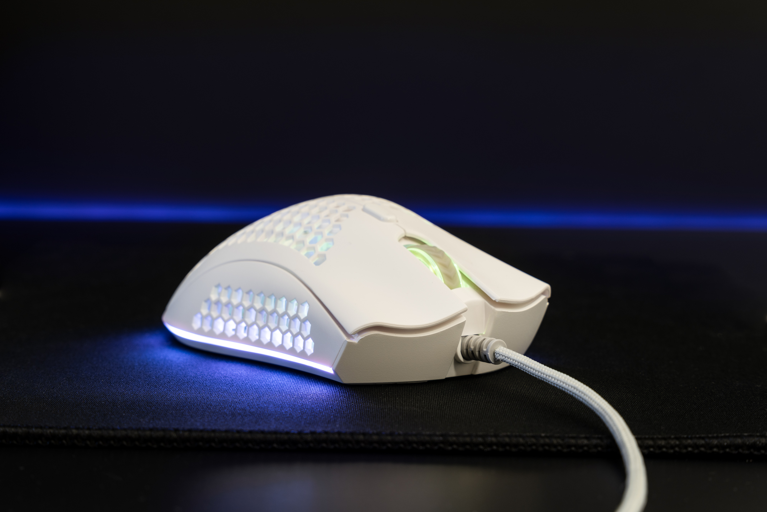 Mouse da gaming bianco con design a nido d'ape. Ha un cavo ed è su un tappetino nero.